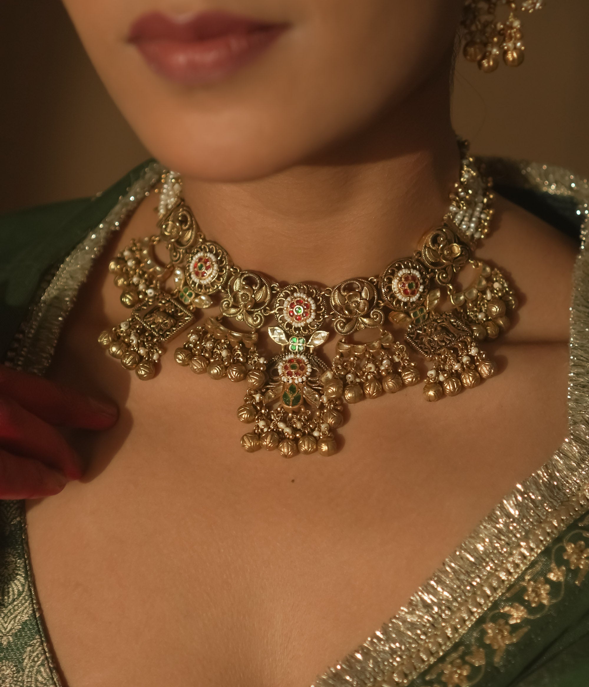 Gold-plated necklace with intricate swirls, red, green, and white gems, pearls, and bells.