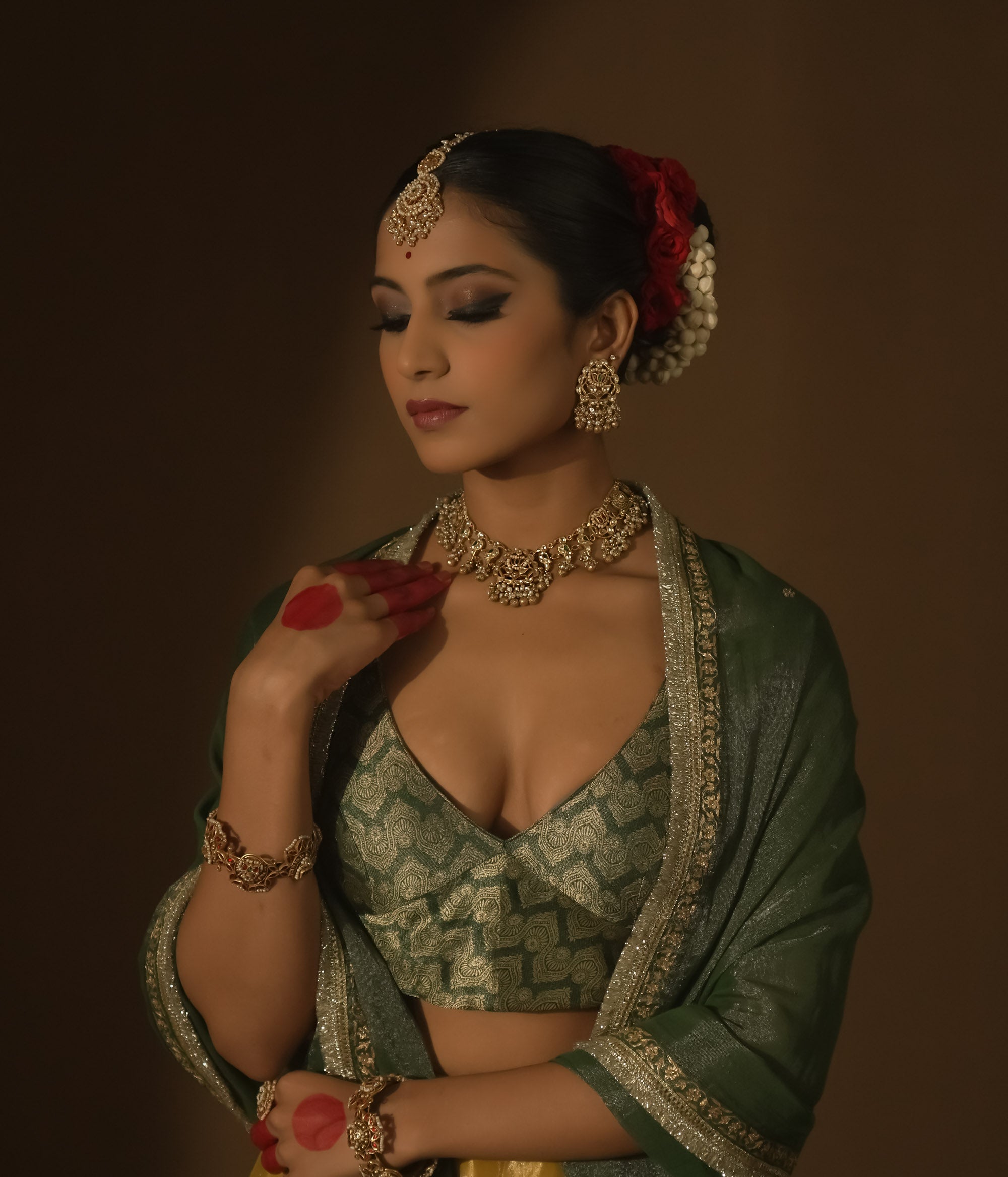 Intricate gold necklace with red and green Kundan stones, pearls, and parrot motifs.