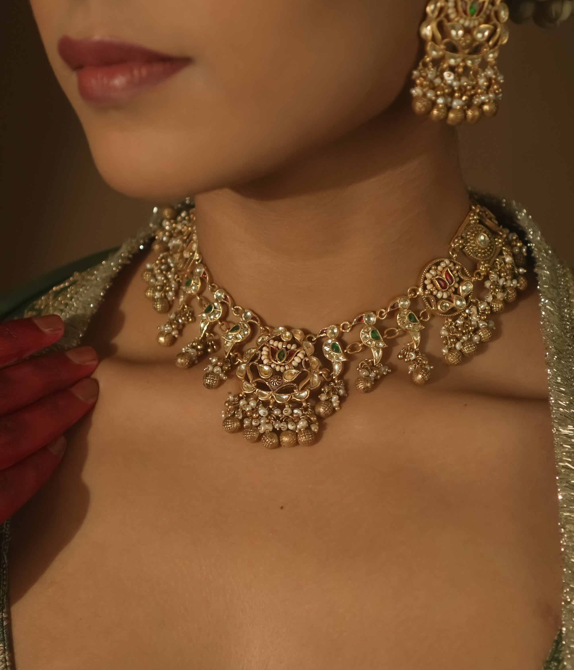 Intricate gold necklace with red and green Kundan stones, pearls, and parrot motifs.