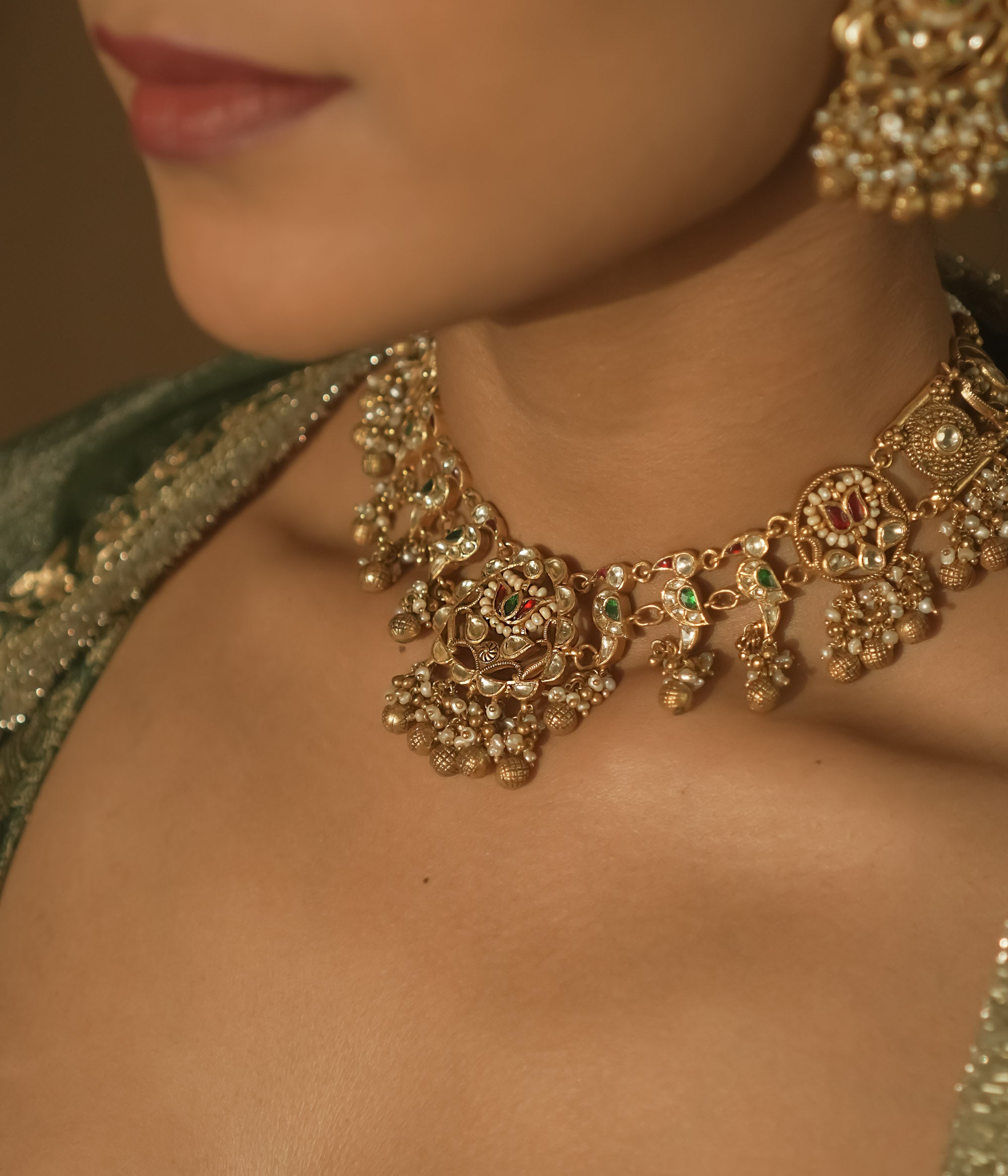 Intricate gold necklace with red and green Kundan stones, pearls, and parrot motifs.