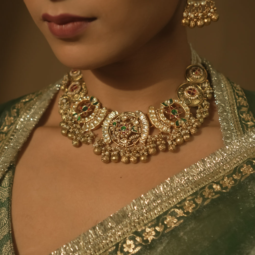 Gold-plated silver necklace with crescent motifs, red, green, and clear Kundan stones, and bells.