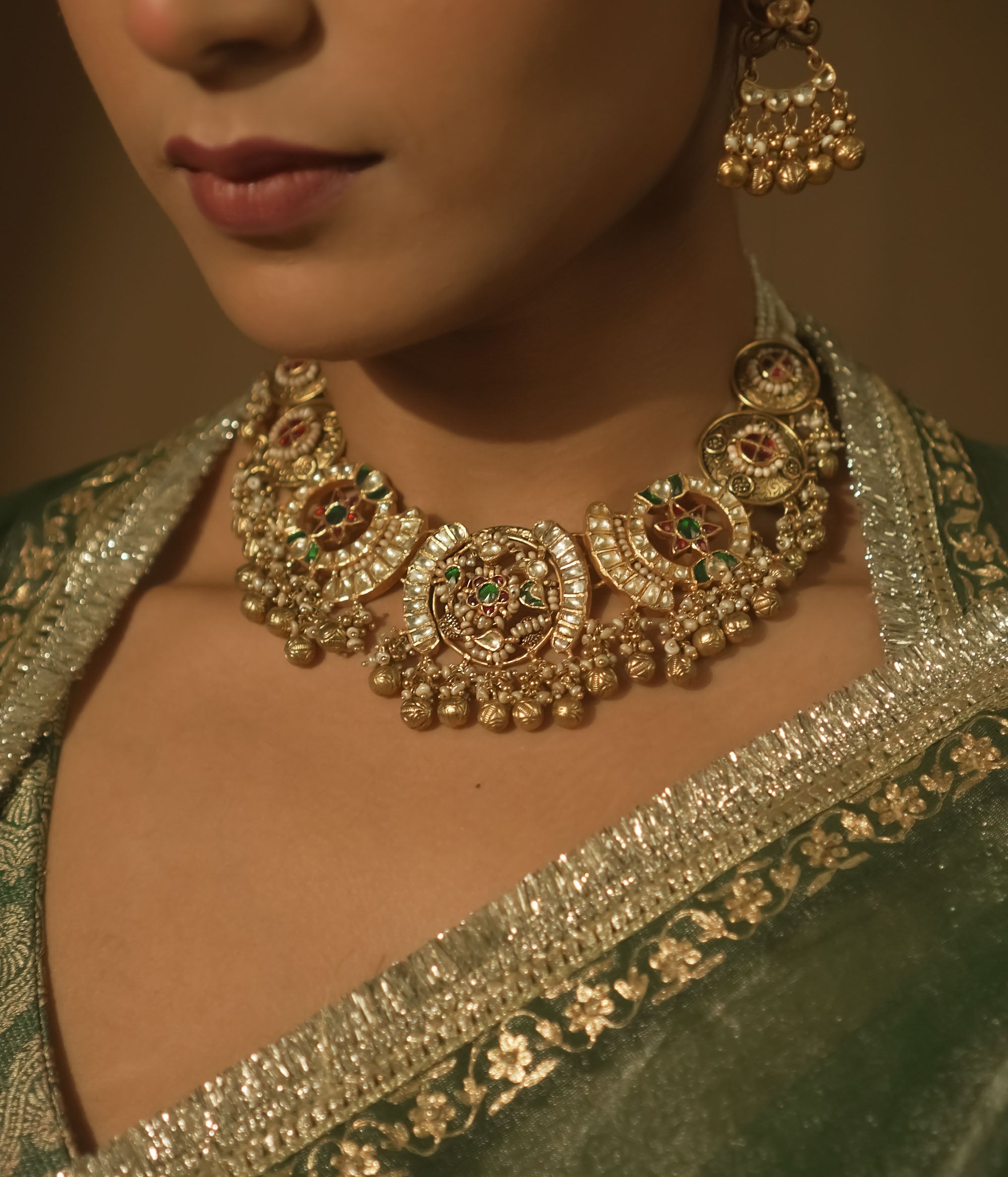 Gold-plated silver necklace with crescent motifs, red, green, and clear Kundan stones, and bells.