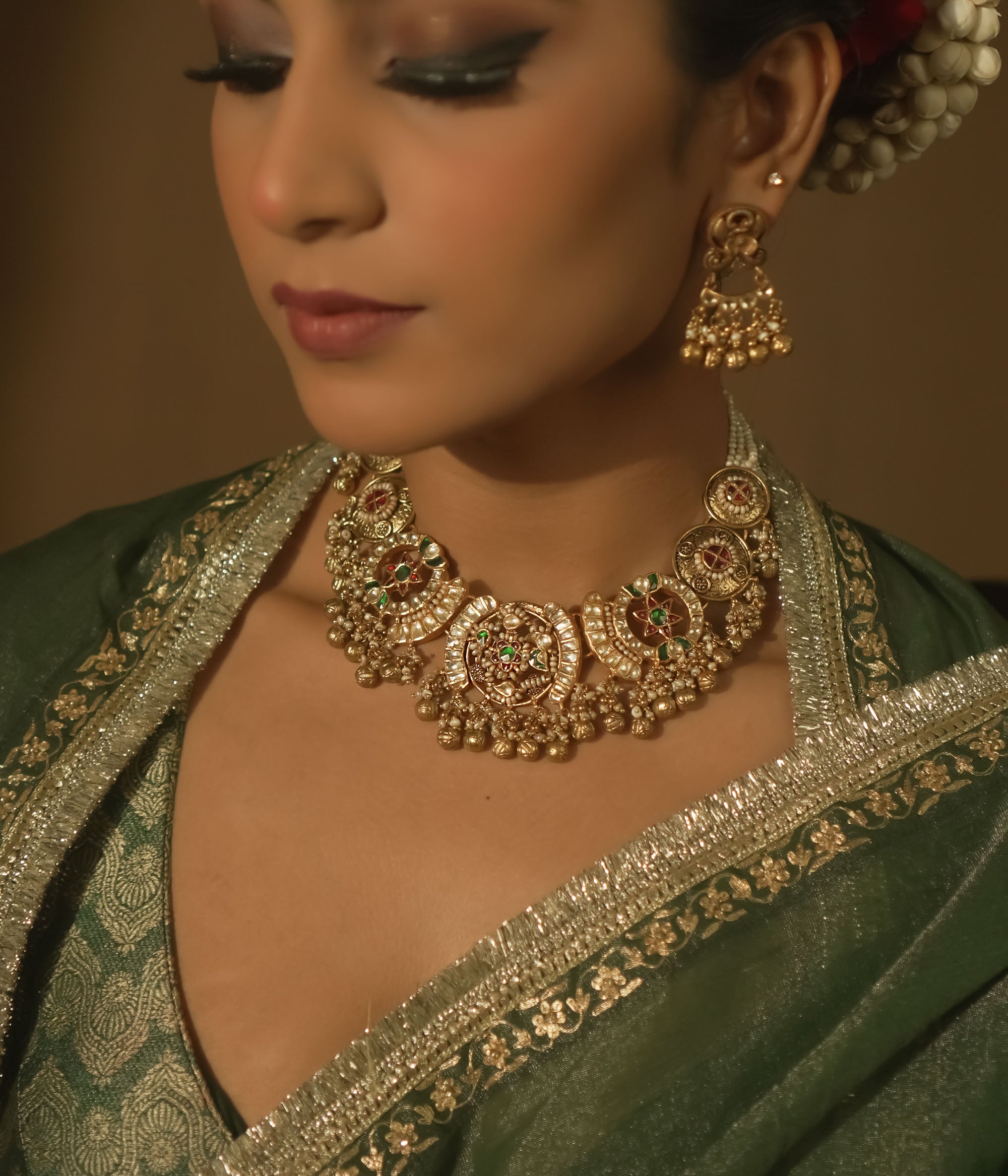 Gold-plated silver necklace with crescent motifs, red, green, and clear Kundan stones, and bells.