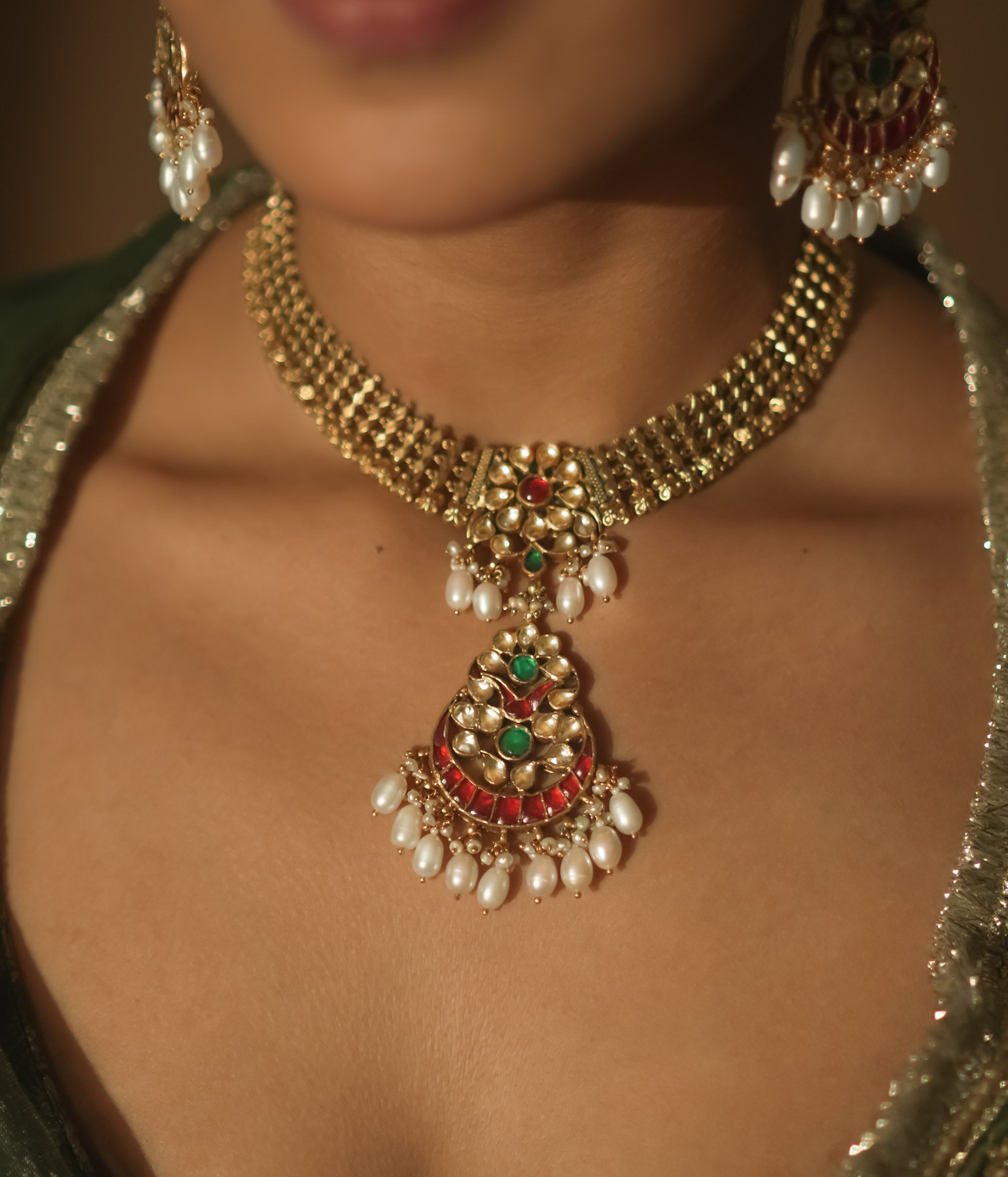 Gold necklace with a central pendant, rubies, emeralds, and dangling pearls.