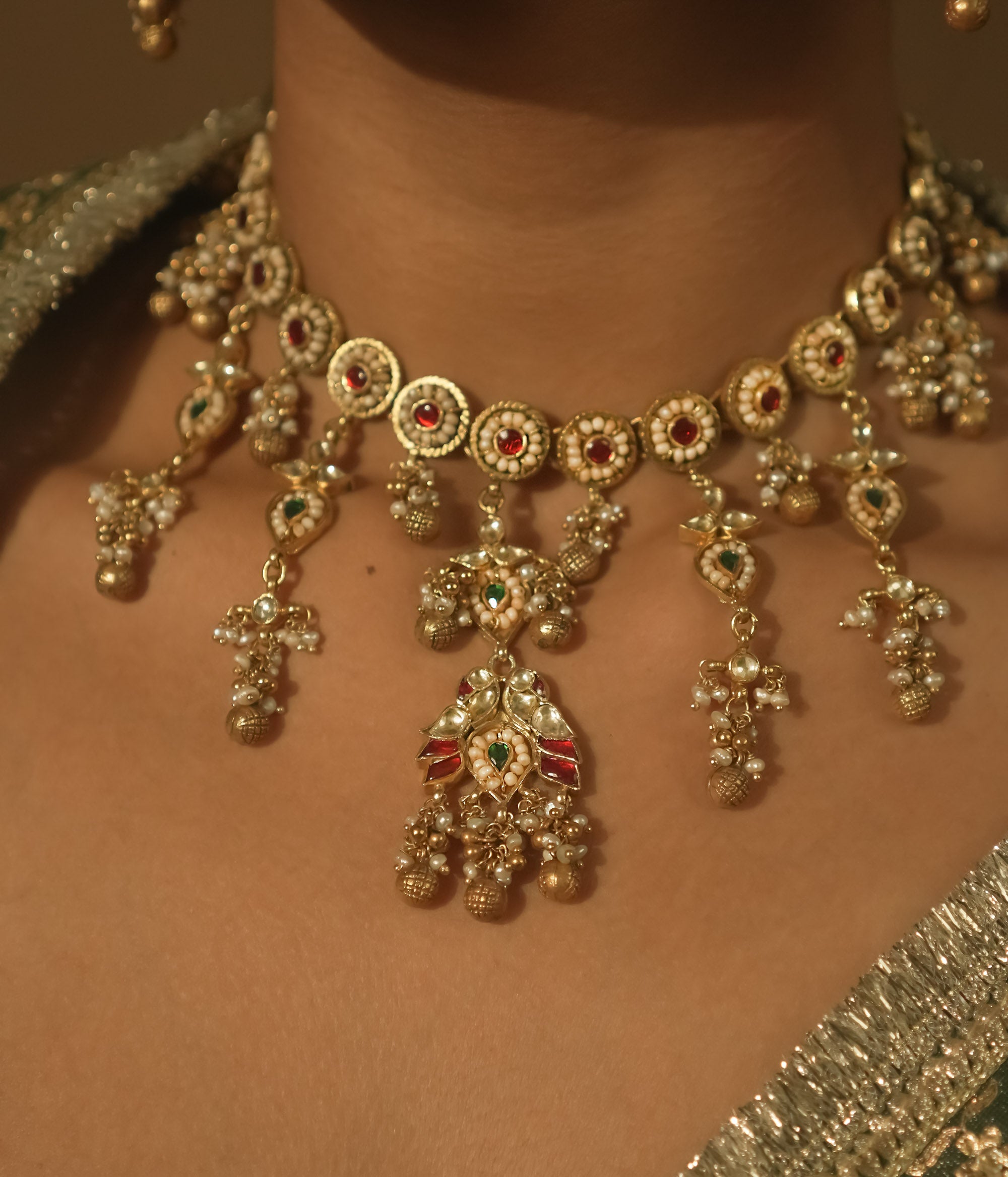 Gold-plated silver necklace with intricate loops, green Kundan, and pearls.
