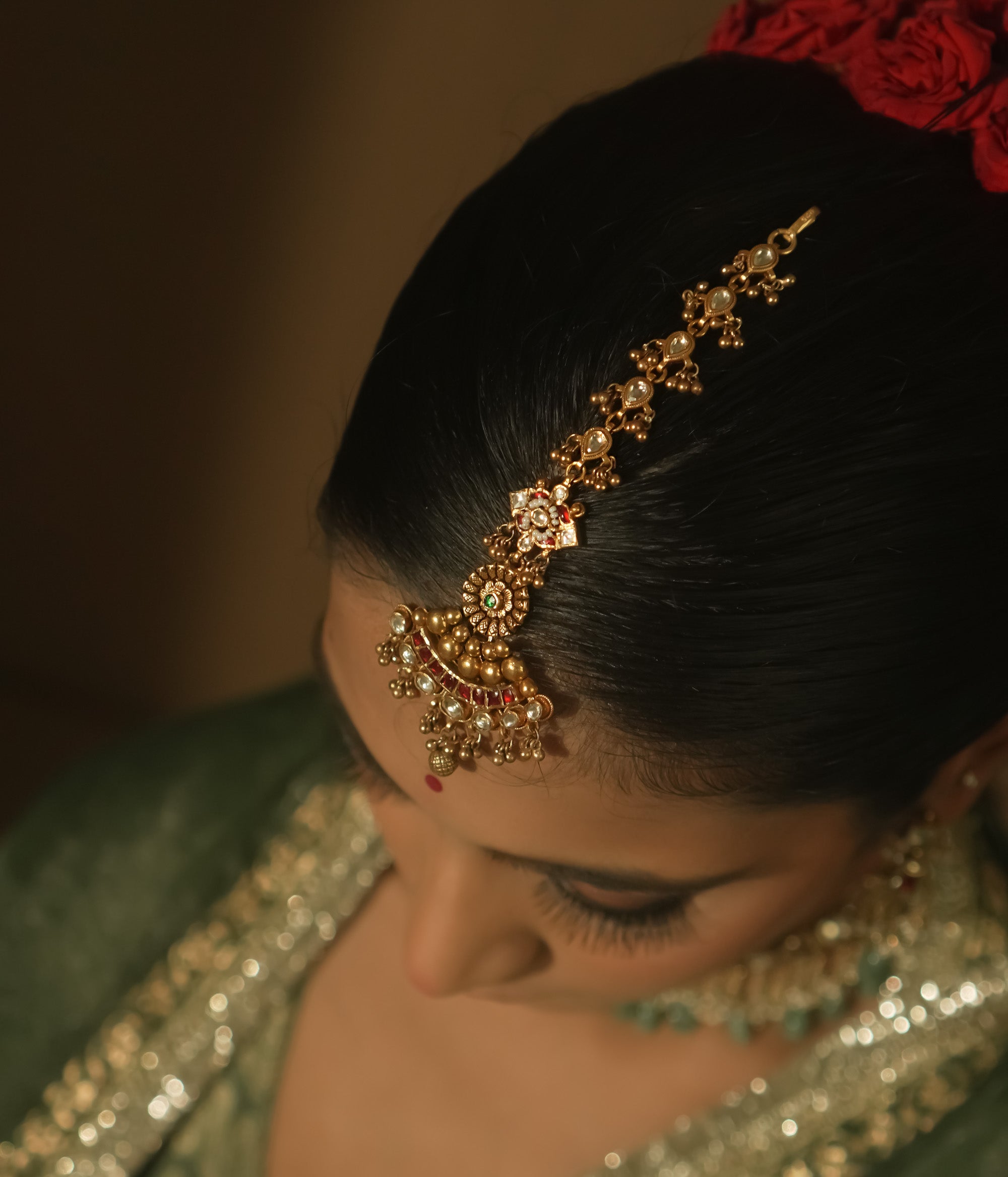 Gold-plated silver maangtika with red, green, and clear Kundan stones and tiny bells.