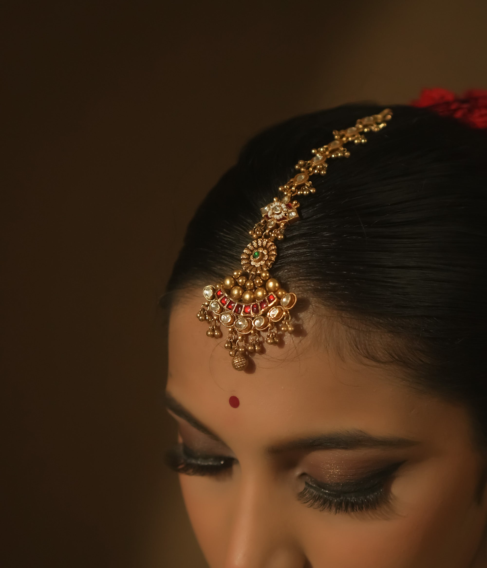 Gold-plated silver maangtika with red, green, and clear Kundan stones and tiny bells.