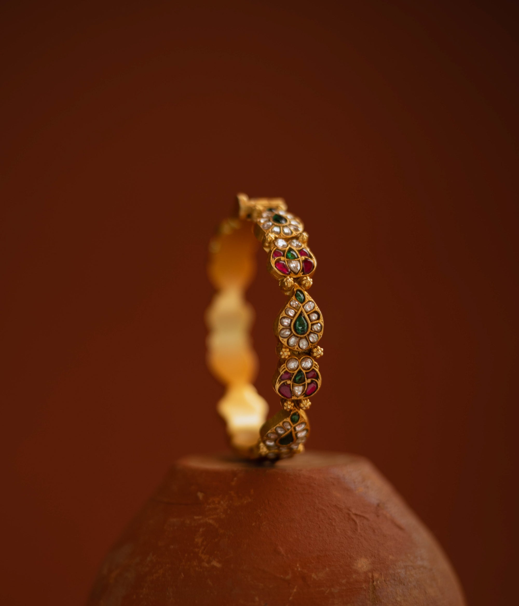 Gold bangle with red, green, and white kundan stones in traditional floral design.