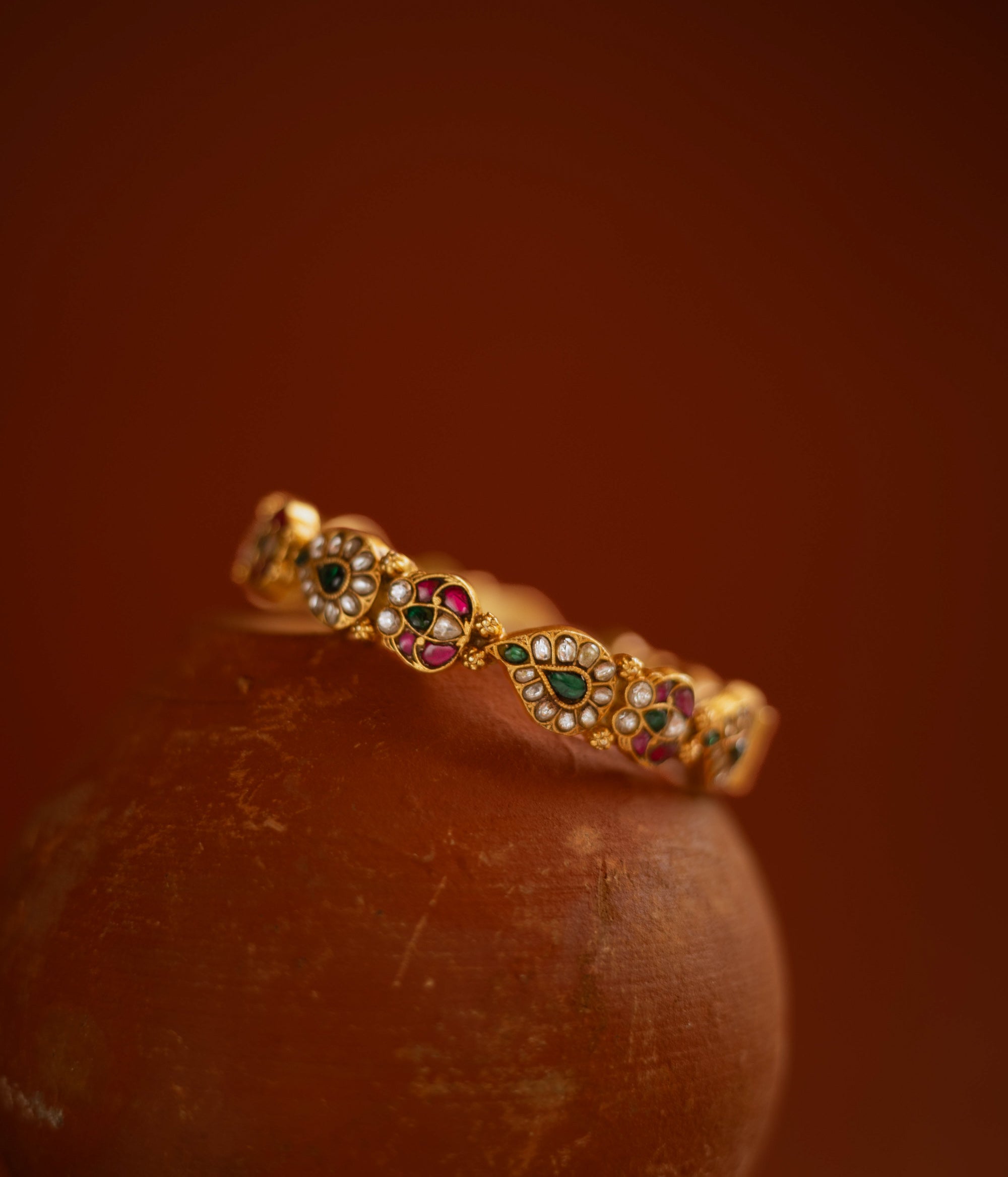 Gold bangle with red, green, and white kundan stones in traditional floral design.