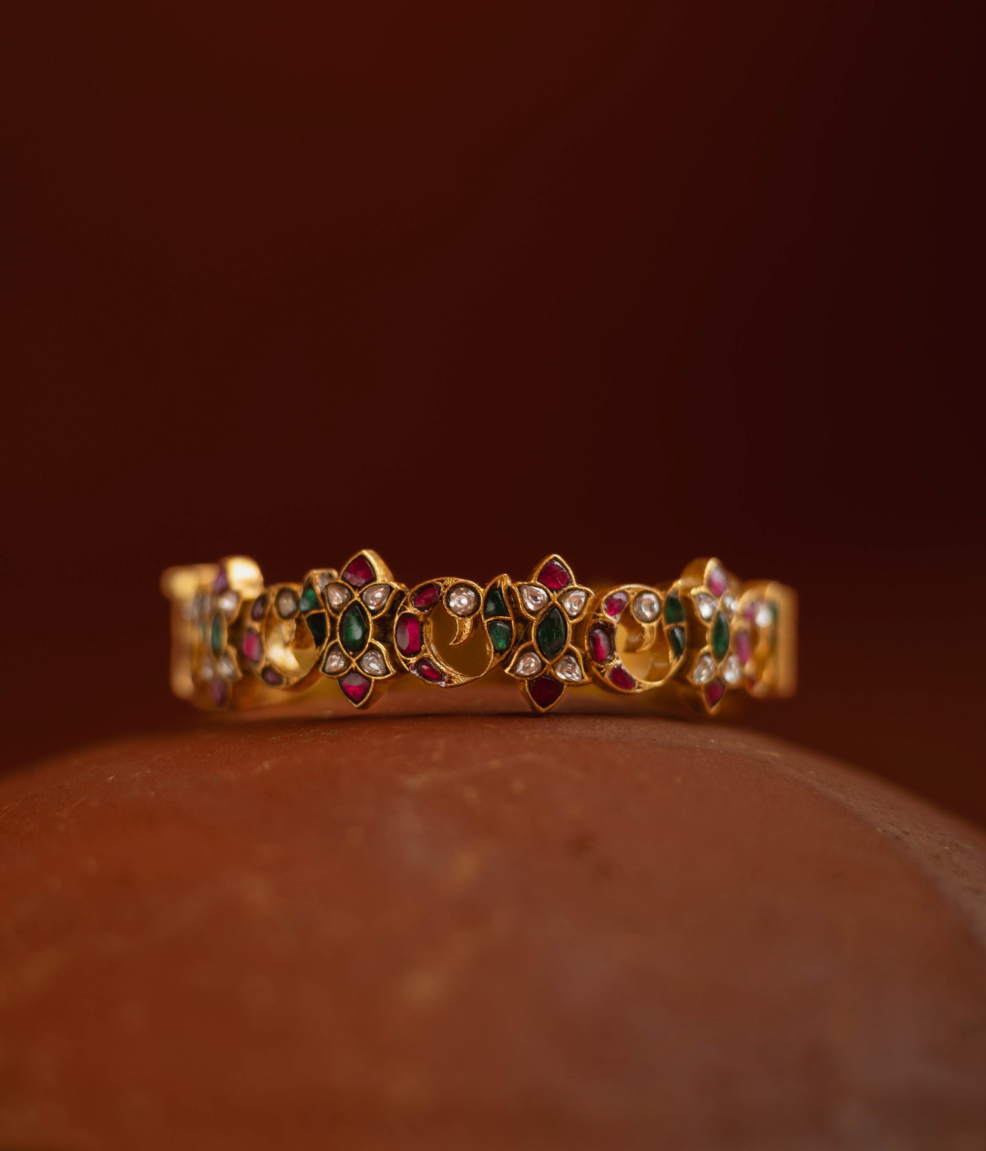 Kundan bangle with alternating moon and floral motifs, set in red, green, white stones.