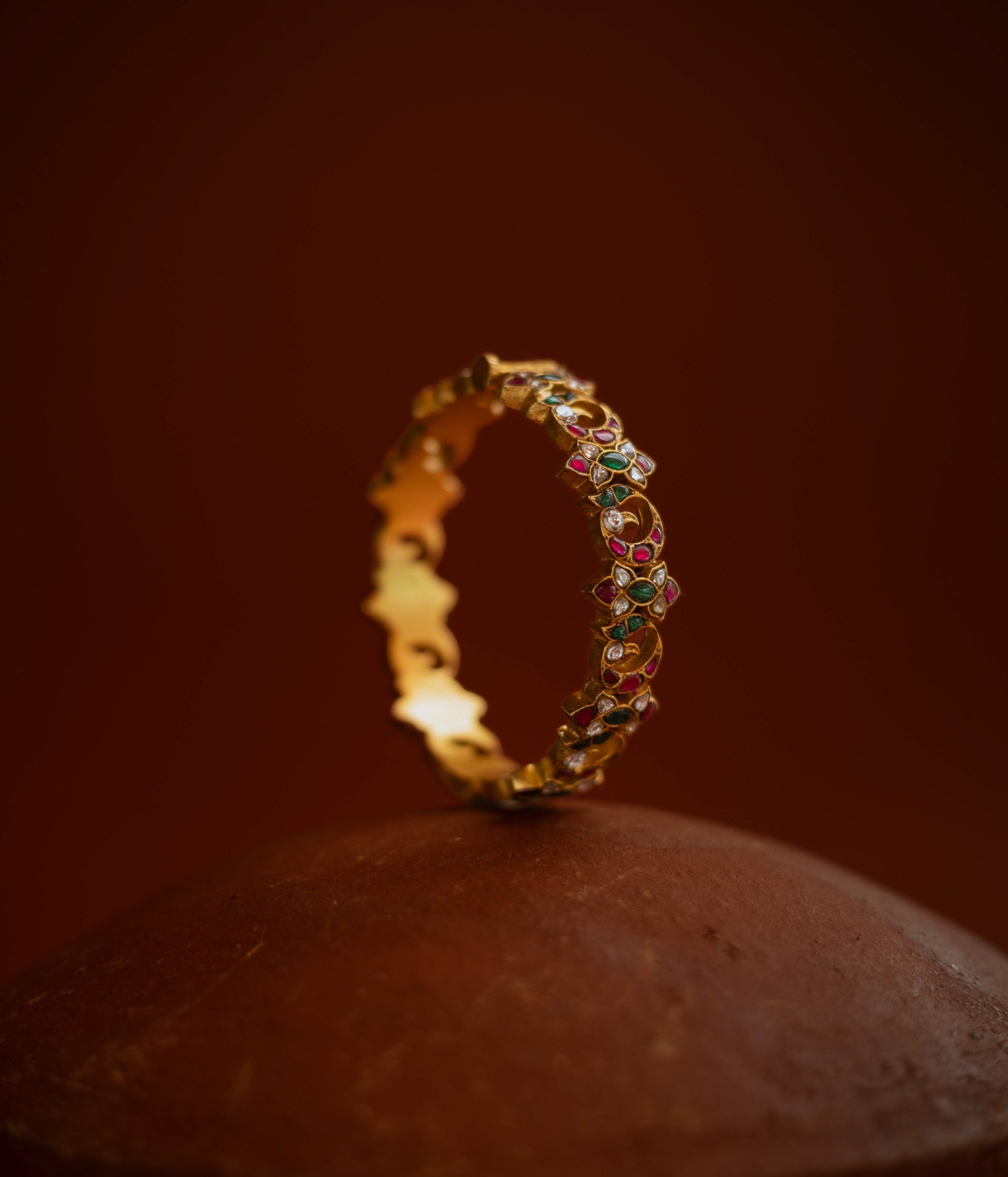 Kundan bangle with alternating moon and floral motifs, set in red, green, white stones.