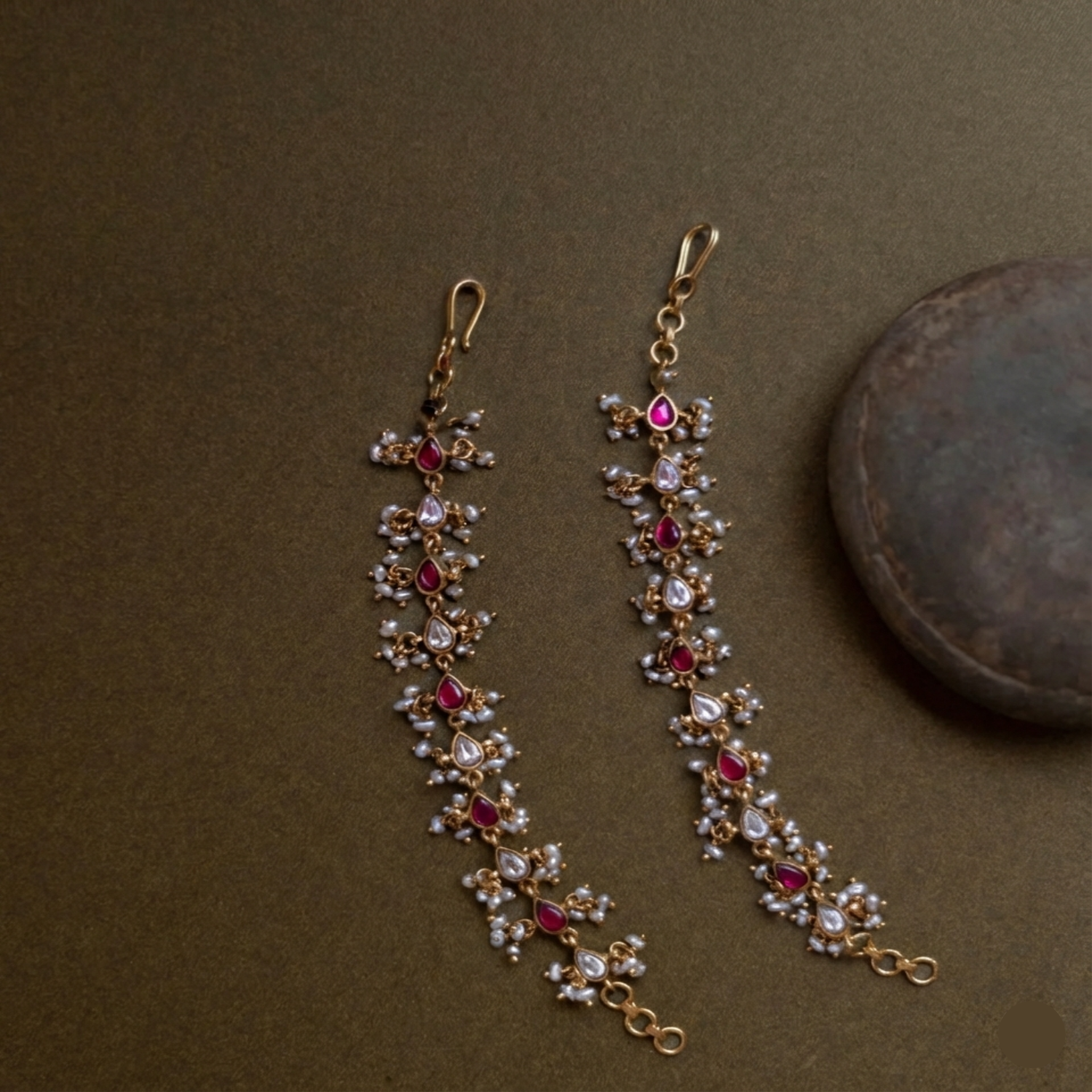 Pair of gold earrings with red and clear gemstones on a brown background