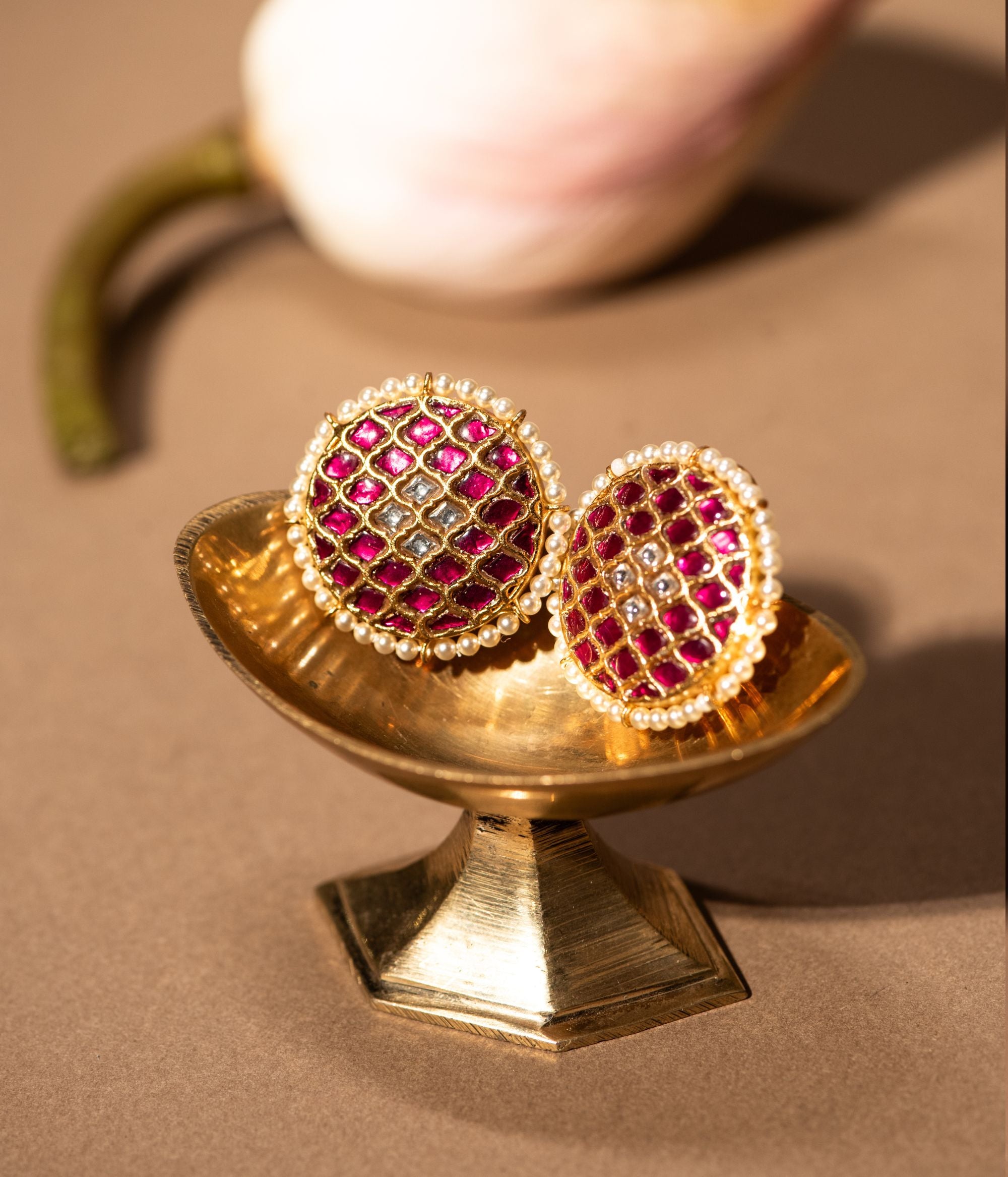 Gold-plated silver round stud earrings featuring a traditional design, adorned with red and white Kundan stones at the center, beautifully surrounded by delicate pearls, adding a timeless and elegant touch.