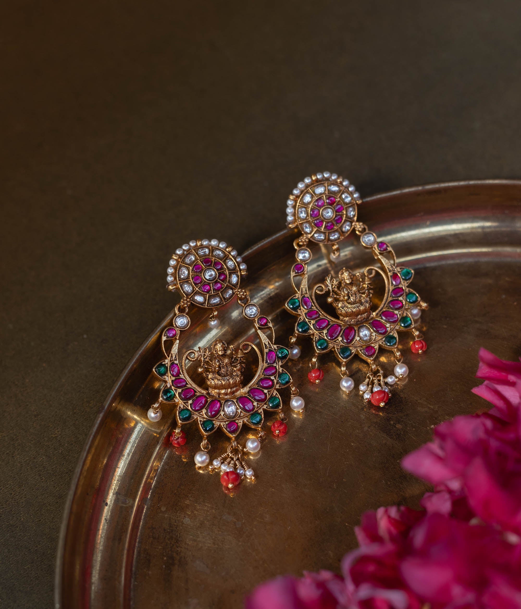 Stunning gold-plated 92.5 sterling silver Lakshmi Chandbali Earrings featuring a crescent moon shape with vibrant red and green Kemp stones, sparkling white stones, and a central Goddess Lakshmi motif. Delicate pearls and coral beads dangle from the lower edge, perfect for festive occasions and weddings.