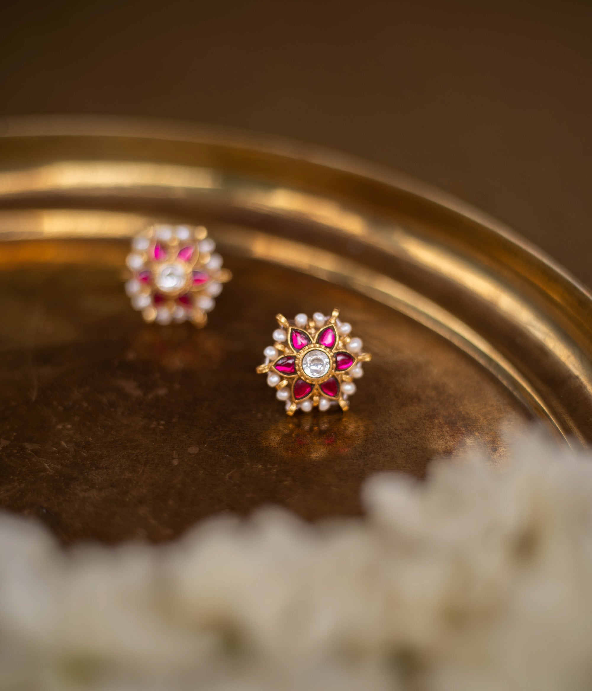 Meira Kundan Earrings with red and white kundan stones and pearl accents on a floral base, placed on a golden brass surface.