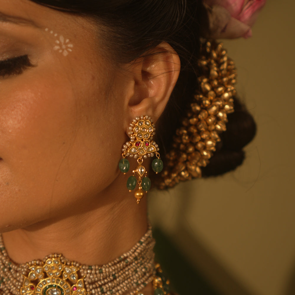 Gold-toned Kundan earrings with red and white stones, green bead drops, and pearl accents—traditional and regal design.