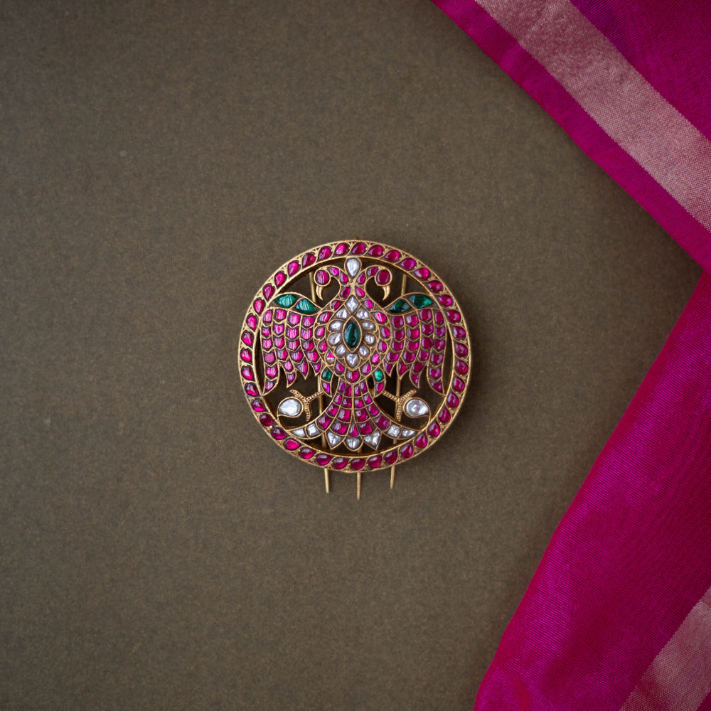 Bird motif Nayika Kundan Hairpin with red, white, and green kundan stones placed on a dark surface with pink silk fabric.
