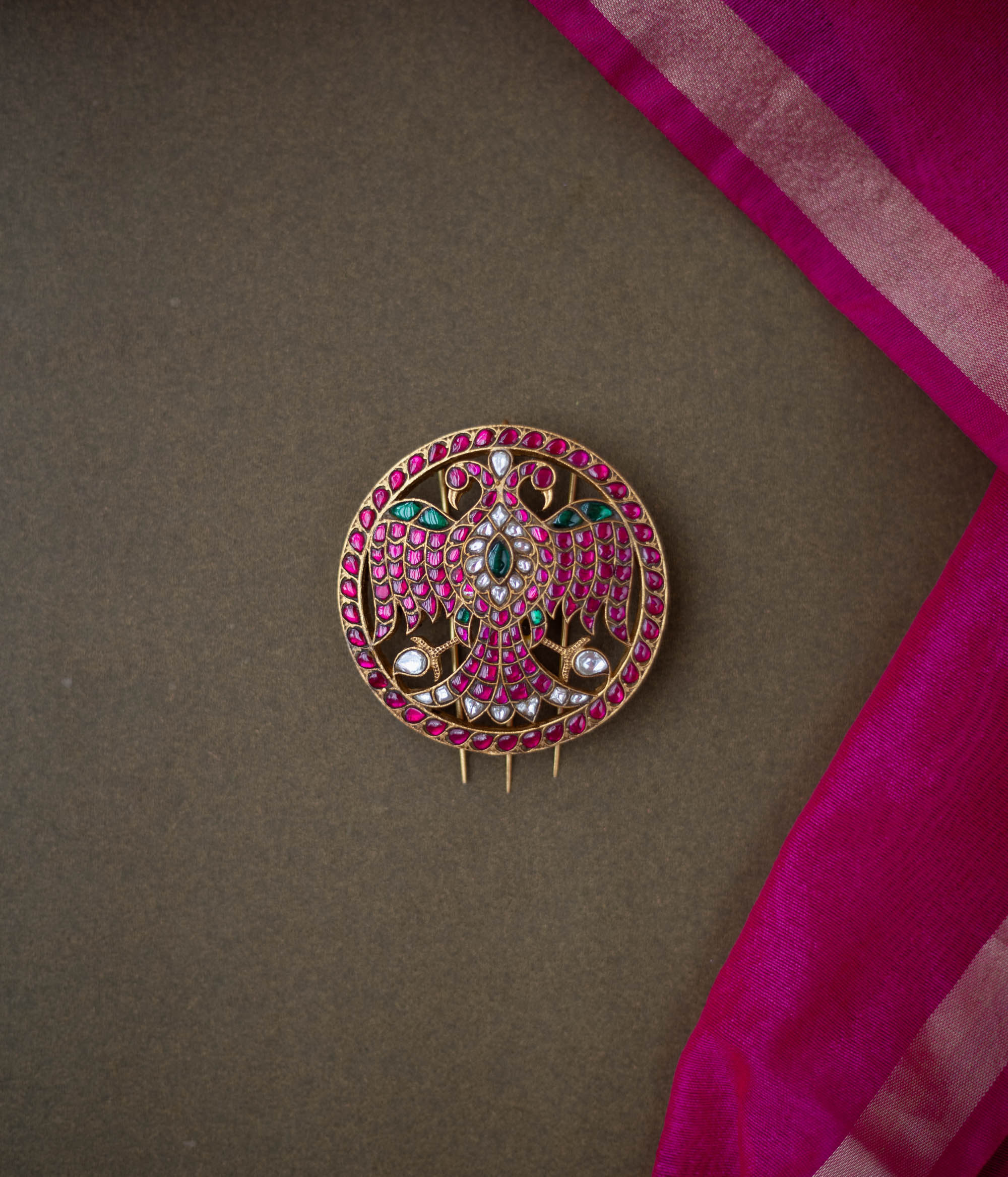 Bird motif Nayika Kundan Hairpin with red, white, and green kundan stones placed on a dark surface with pink silk fabric.
