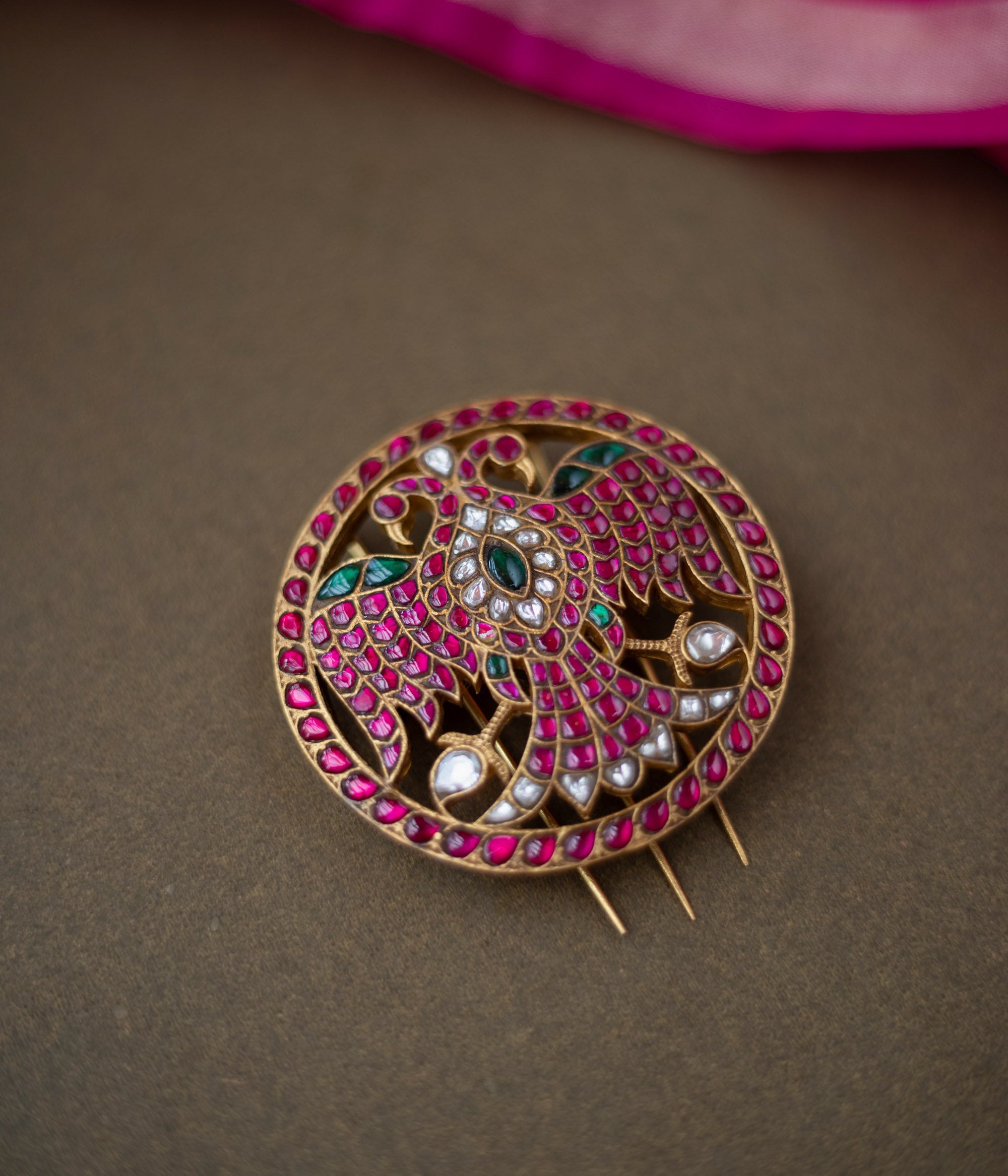 Bird motif Nayika Kundan Hairpin with red, white, and green kundan stones placed on a dark surface with pink silk fabric.