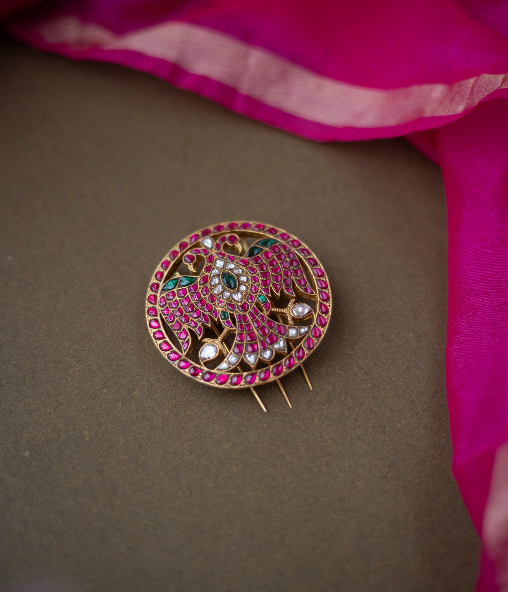 Bird motif Nayika Kundan Hairpin with red, white, and green kundan stones placed on a dark surface with pink silk fabric.