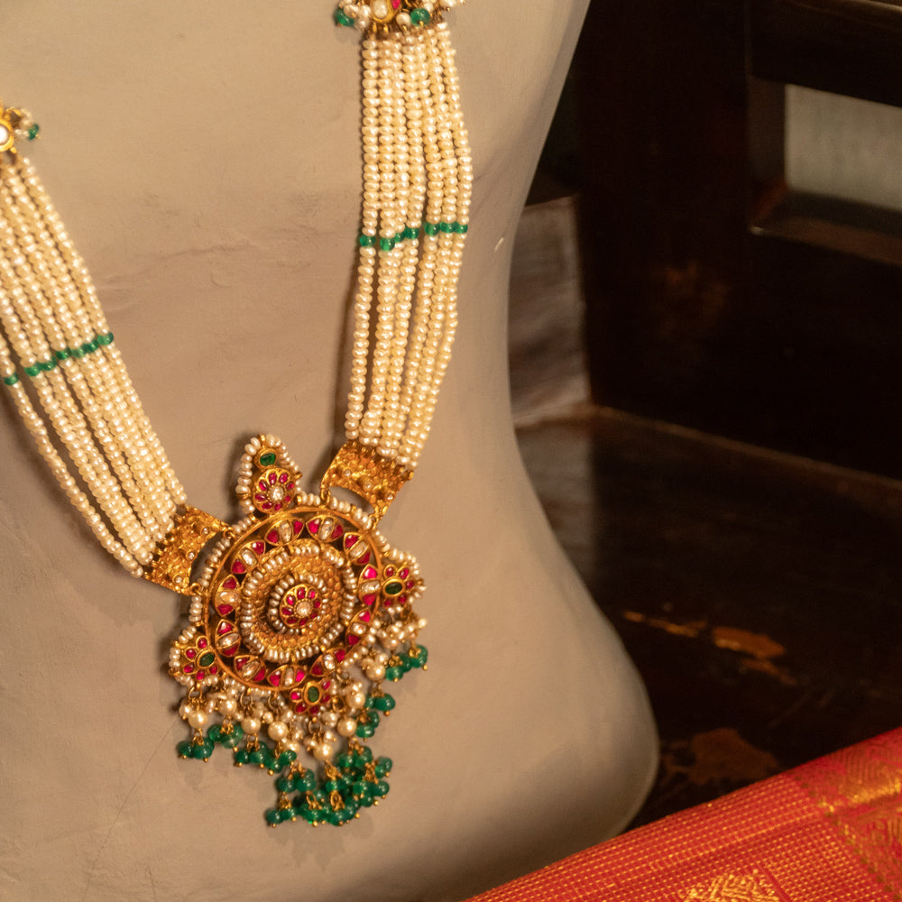 Pearl-string Kundan necklace with circular pendant, red and green stones, and green bead hangings.