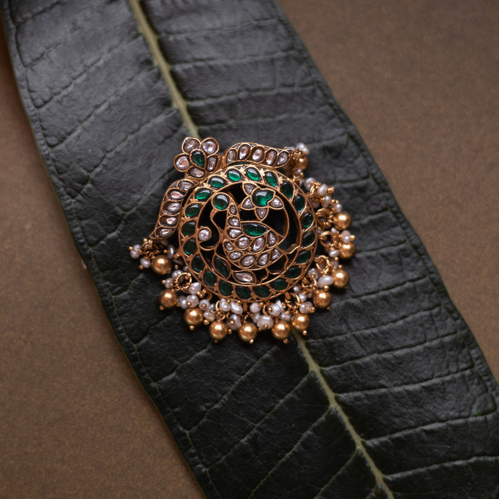 Circular kundan pendant featuring twin peacocks with green and white stones and pearl fringe.