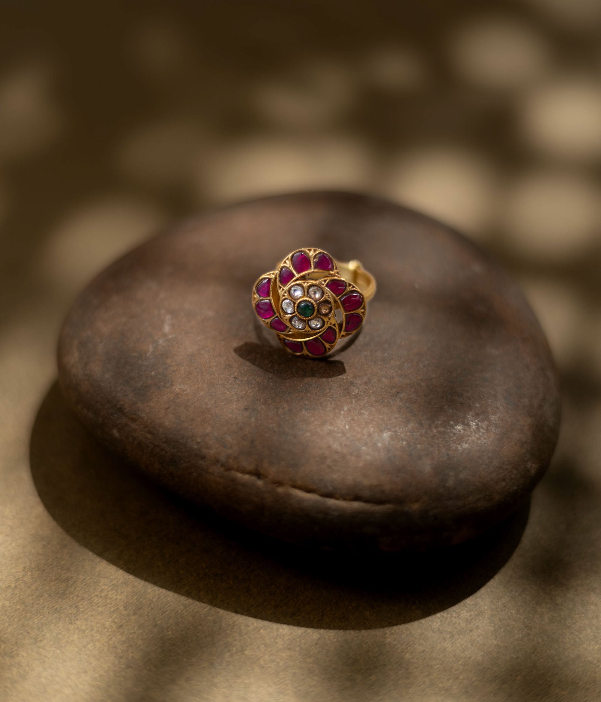 Detailed view of a golden ring. Magenta, ruby, and green stones form a floral design in Kundan style.