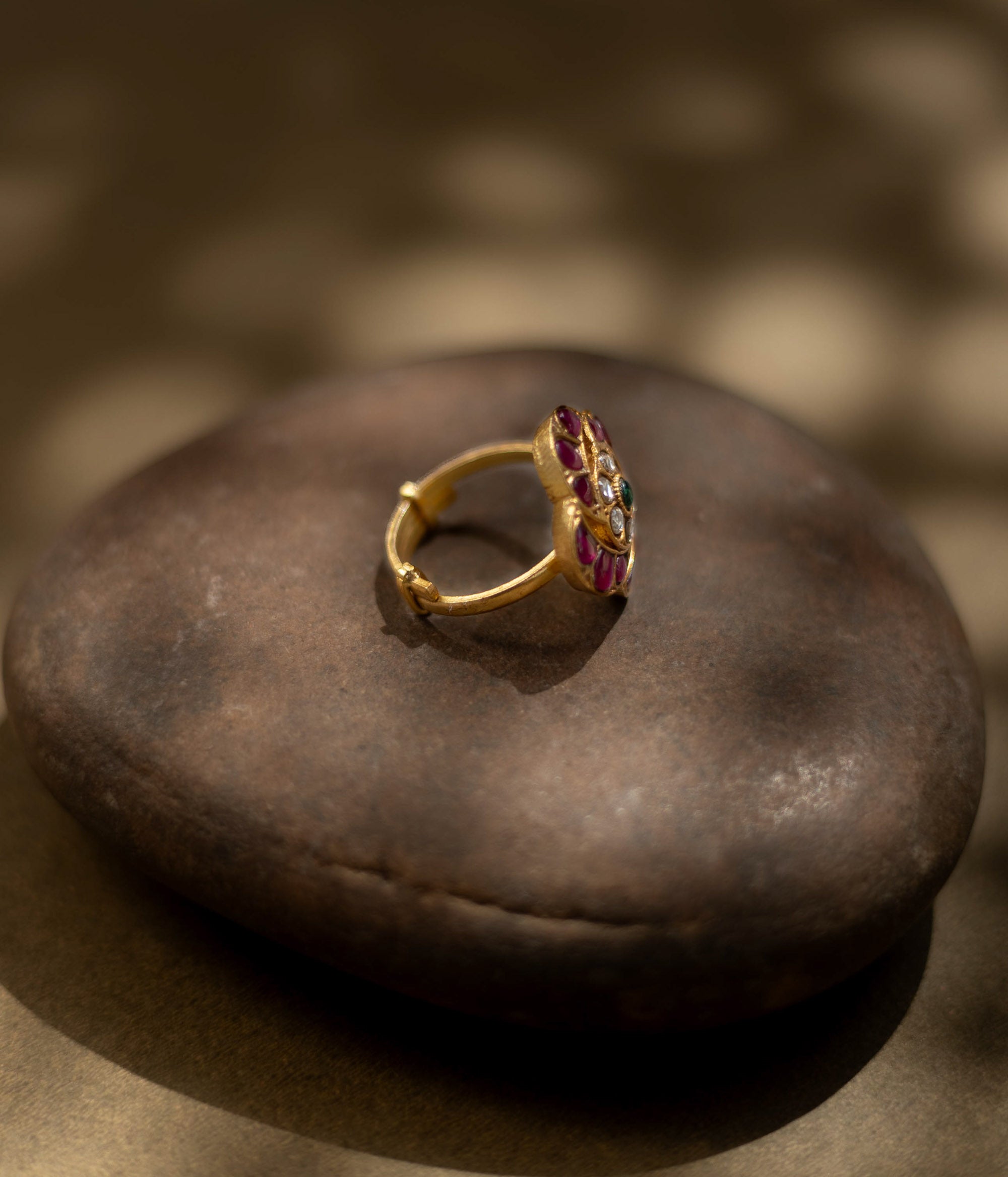 Detailed view of a golden ring. Magenta, ruby, and green stones form a floral design in Kundan style.