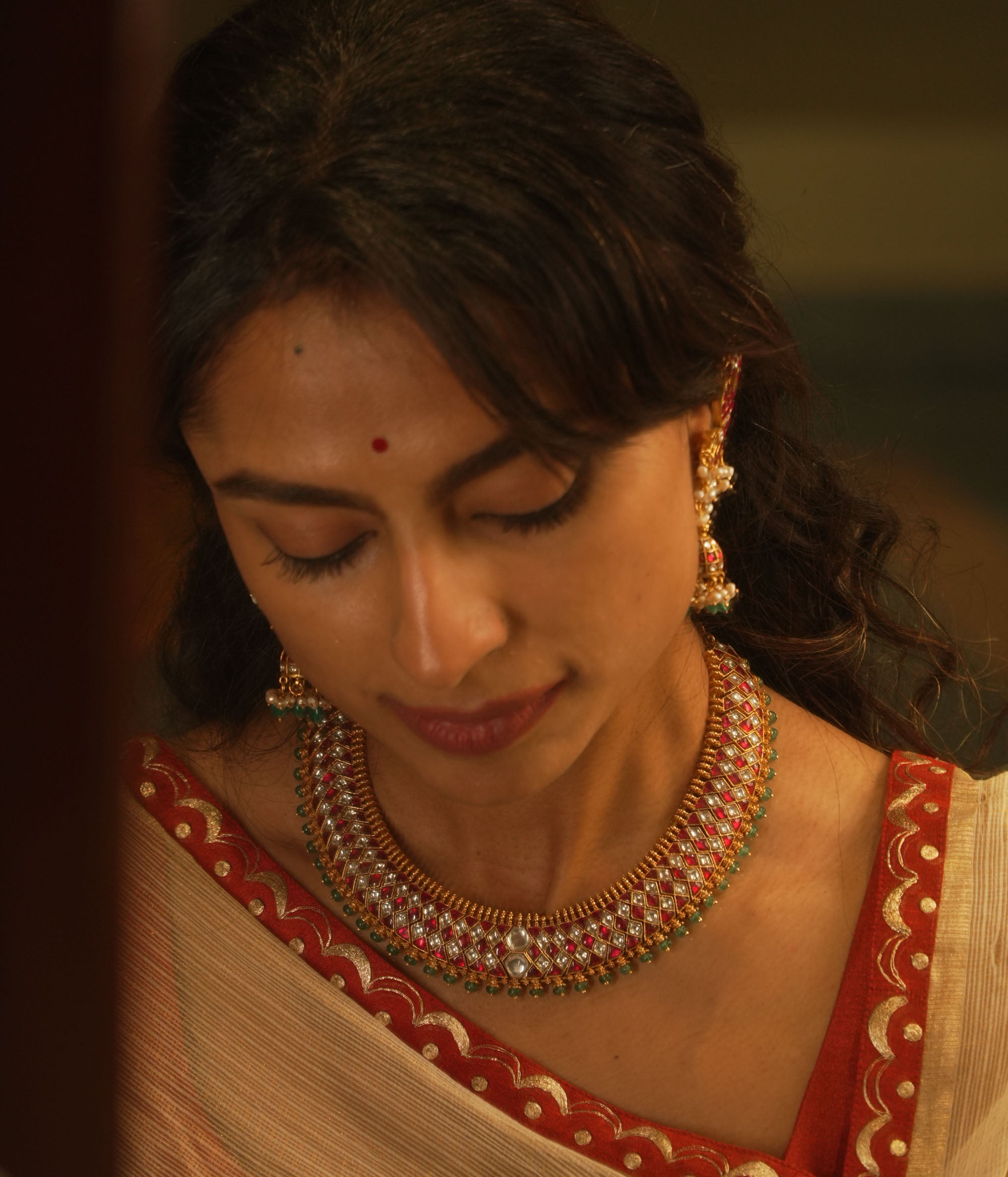 Gold Kundan necklace with red and white kundan stones, and green beads, on a woman's neck.