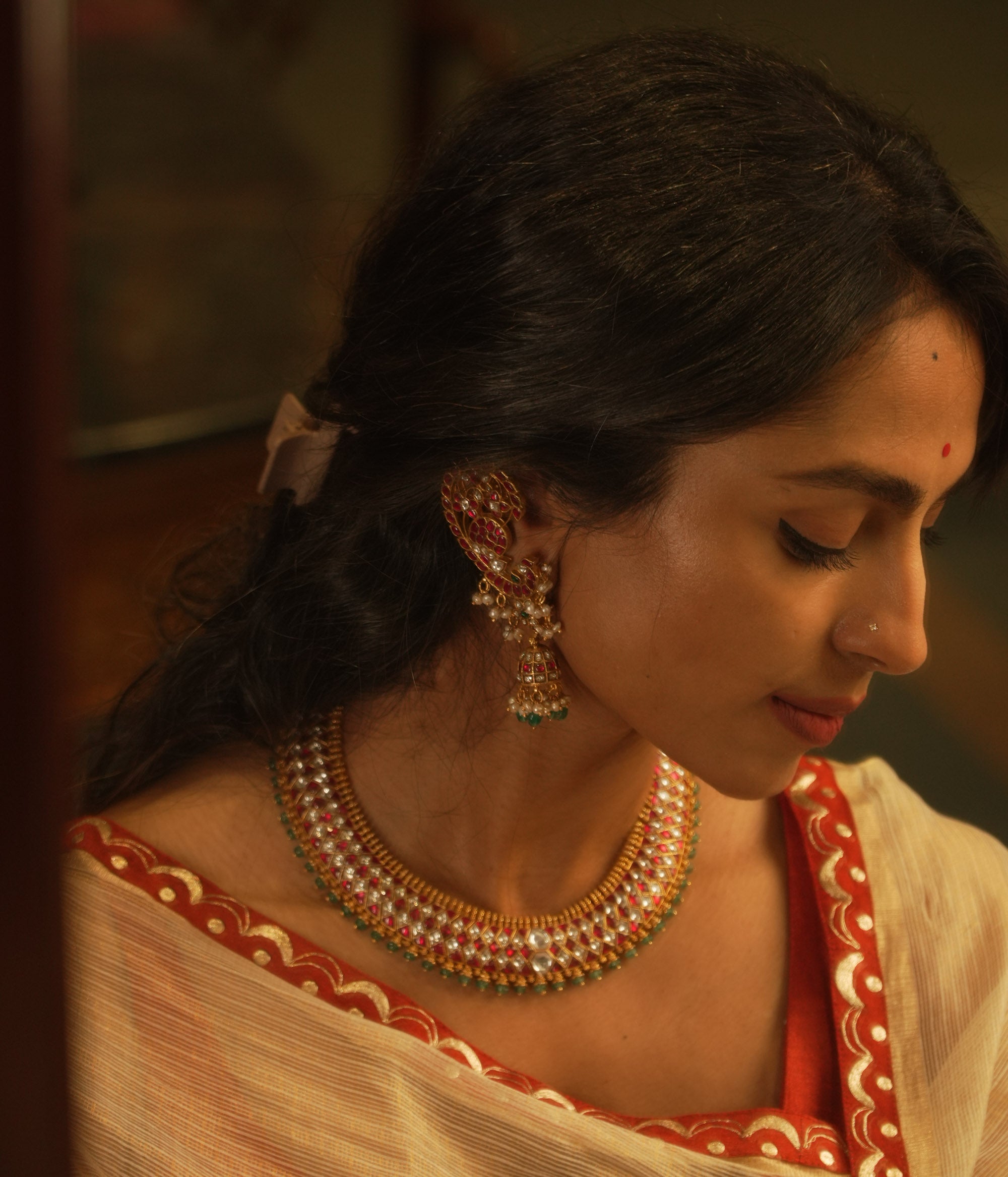 Gold Kundan necklace with red and white kundan stones, and green beads, on a woman's neck.