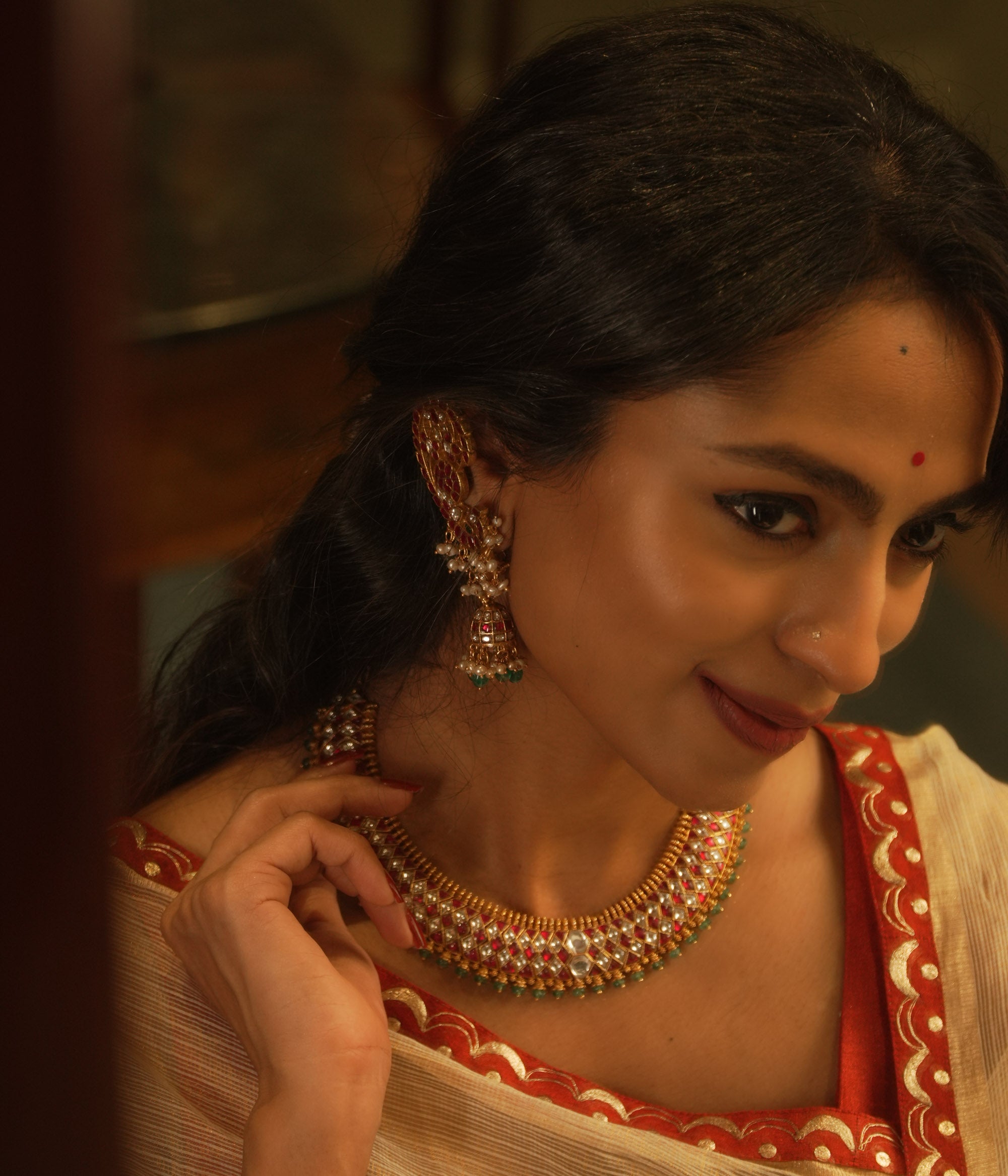 Gold Kundan necklace with red and white kundan stones, and green beads, on a woman's neck.