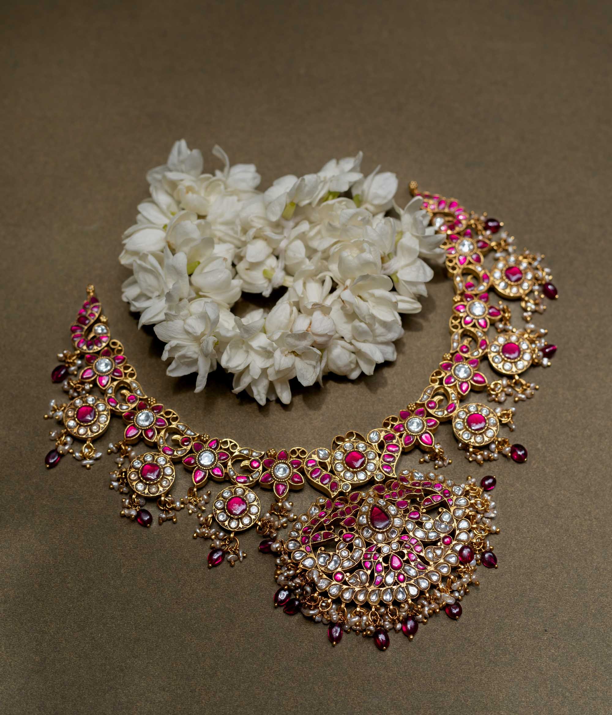 A handcrafted 22ct gold-plated 92.5 sterling silver Rani Haar Kemp Necklace, featuring red, green, and white Kundan stones, red beads, and pearls, with a long, multi-stranded design, intricate floral motifs, and a central pearl-clustered pendant, ideal for bridal ensembles and festive occasions.