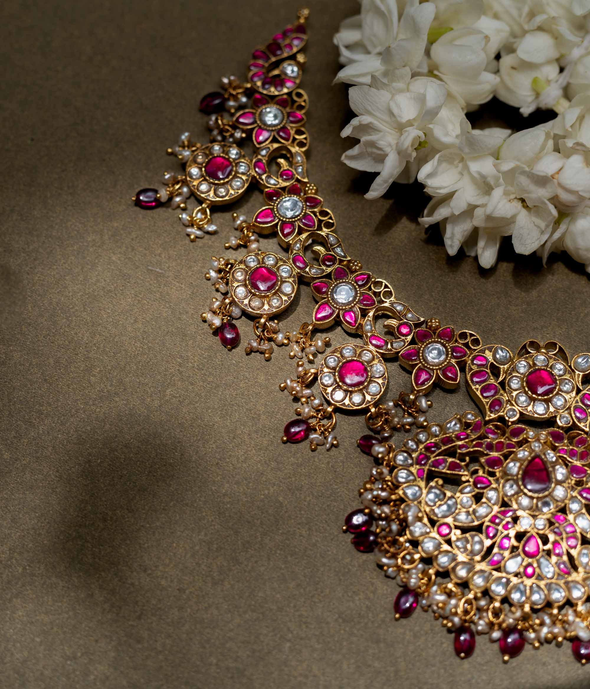 A handcrafted 22ct gold-plated 92.5 sterling silver Rani Haar Kemp Necklace, featuring red, green, and white Kundan stones, red beads, and pearls, with a long, multi-stranded design, intricate floral motifs, and a central pearl-clustered pendant, ideal for bridal ensembles and festive occasions.