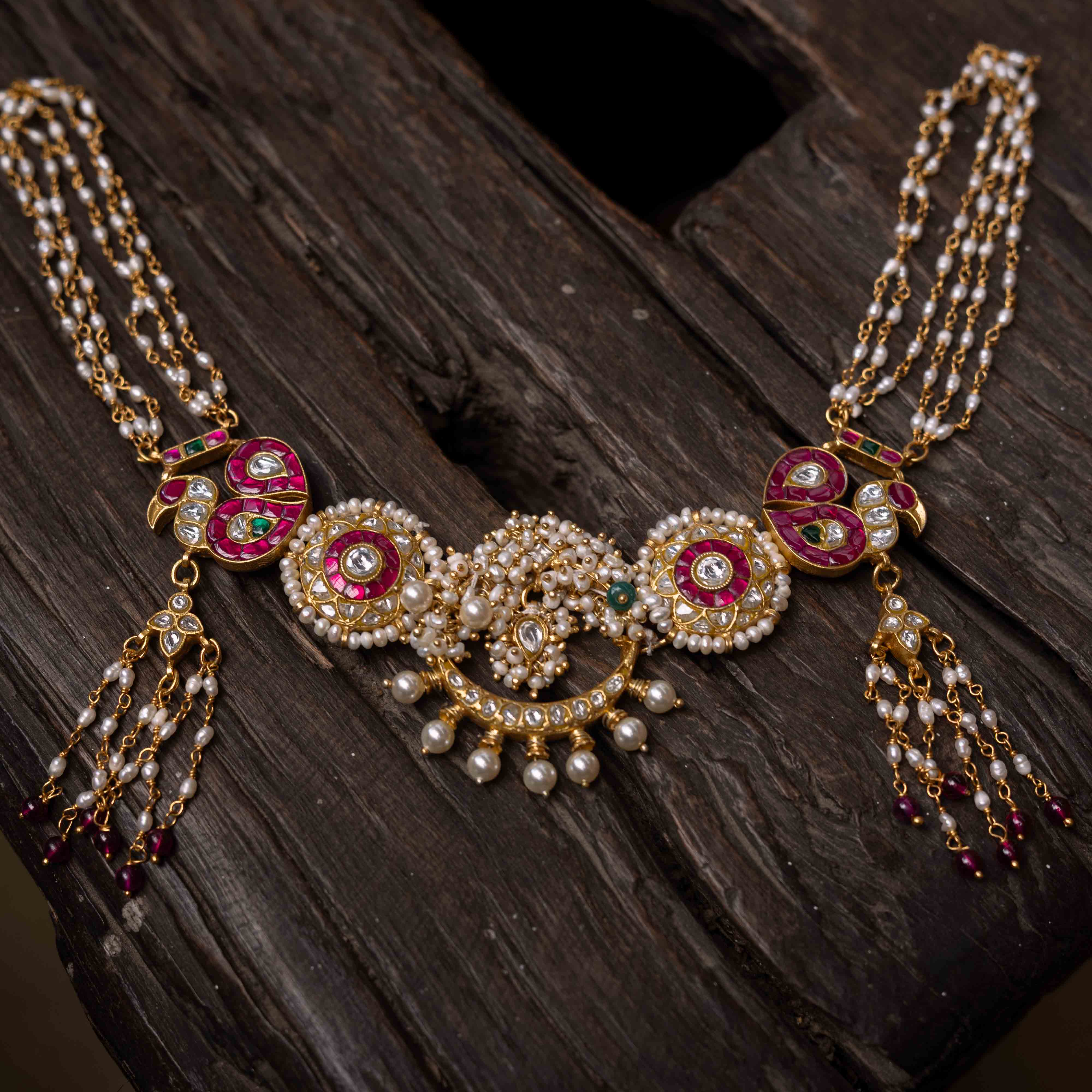 A multi-layered Kundan necklace with a central pendant and cascading strands of red beads and pearls.
