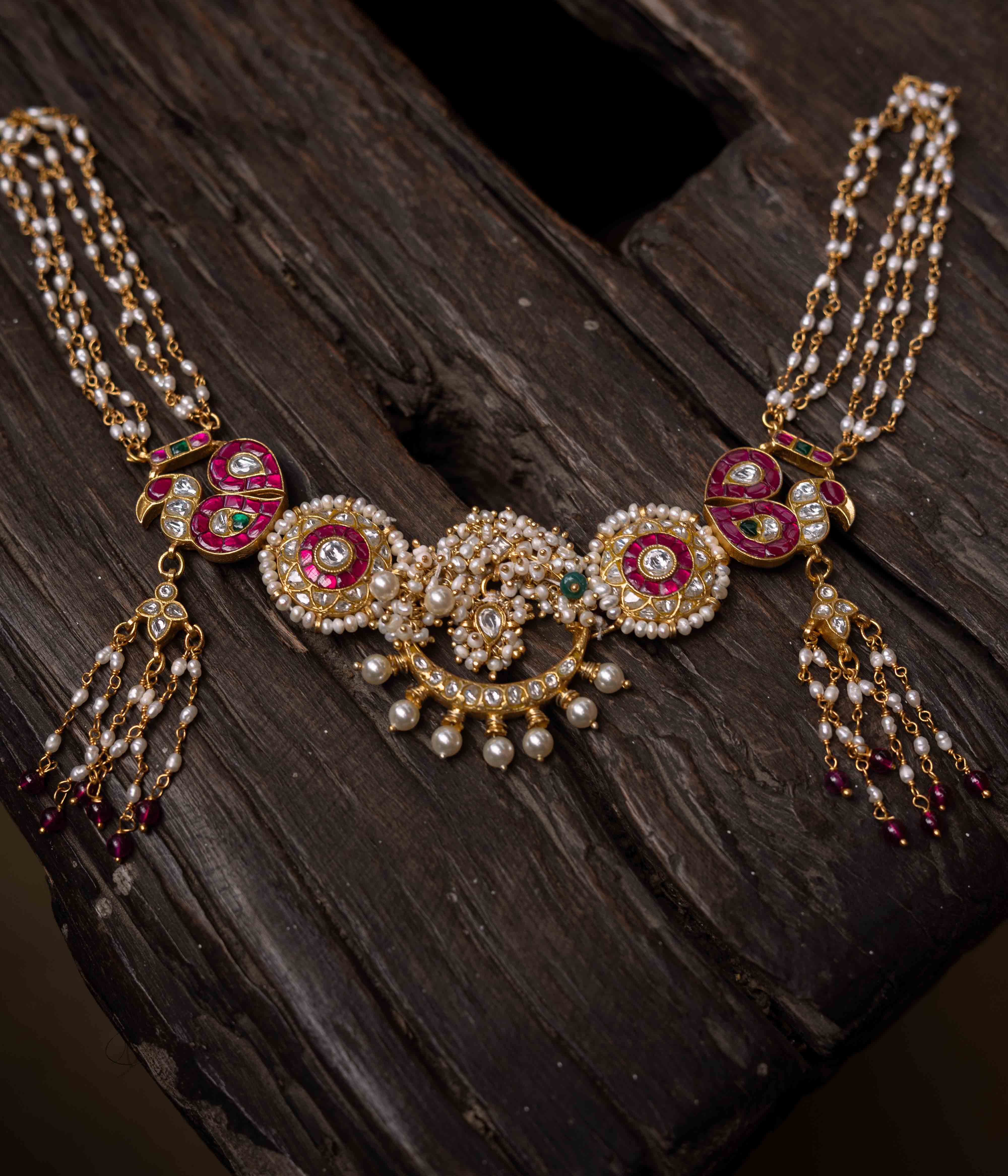 A multi-layered Kundan necklace with a central pendant and cascading strands of red beads and pearls.
