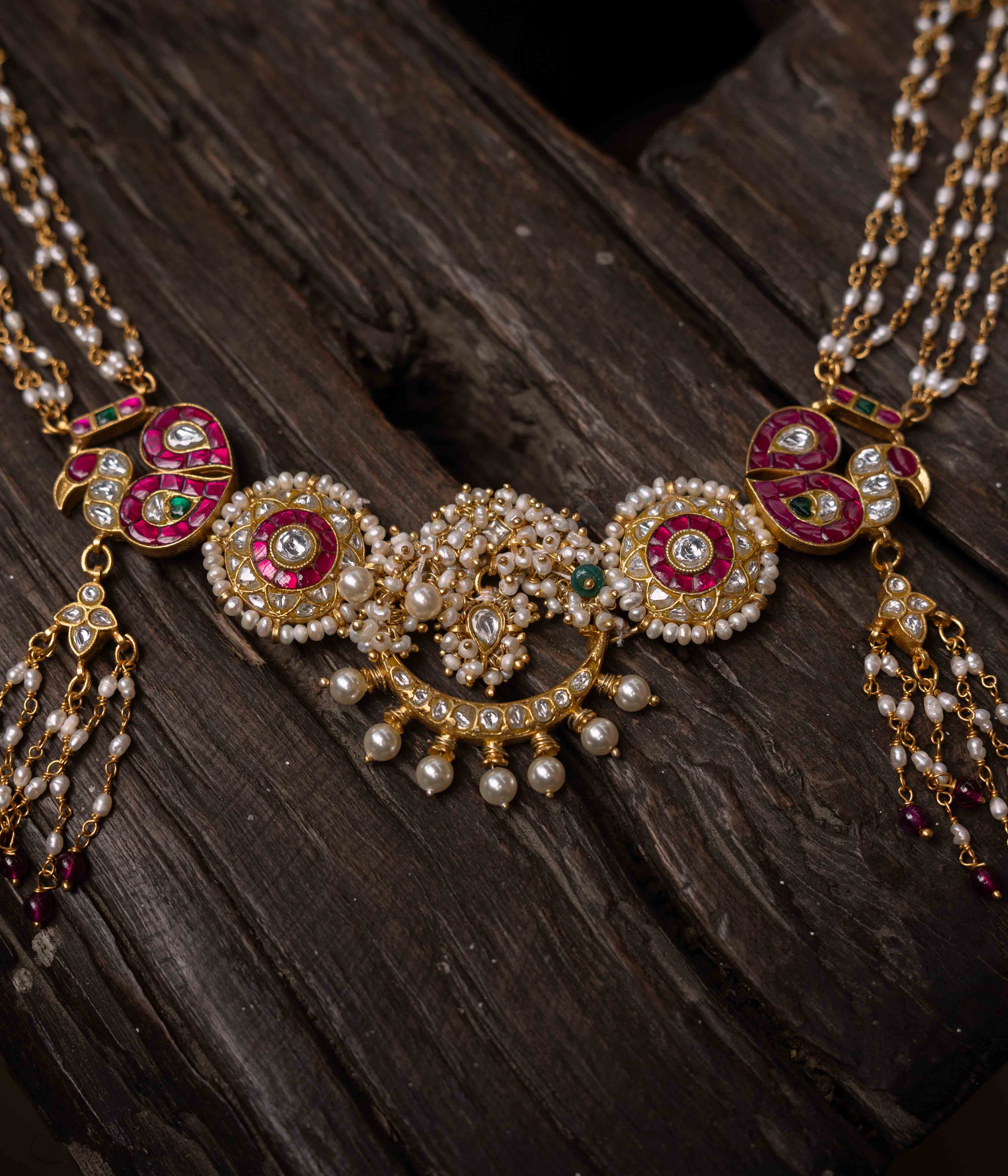 A multi-layered Kundan necklace with a central pendant and cascading strands of red beads and pearls.
