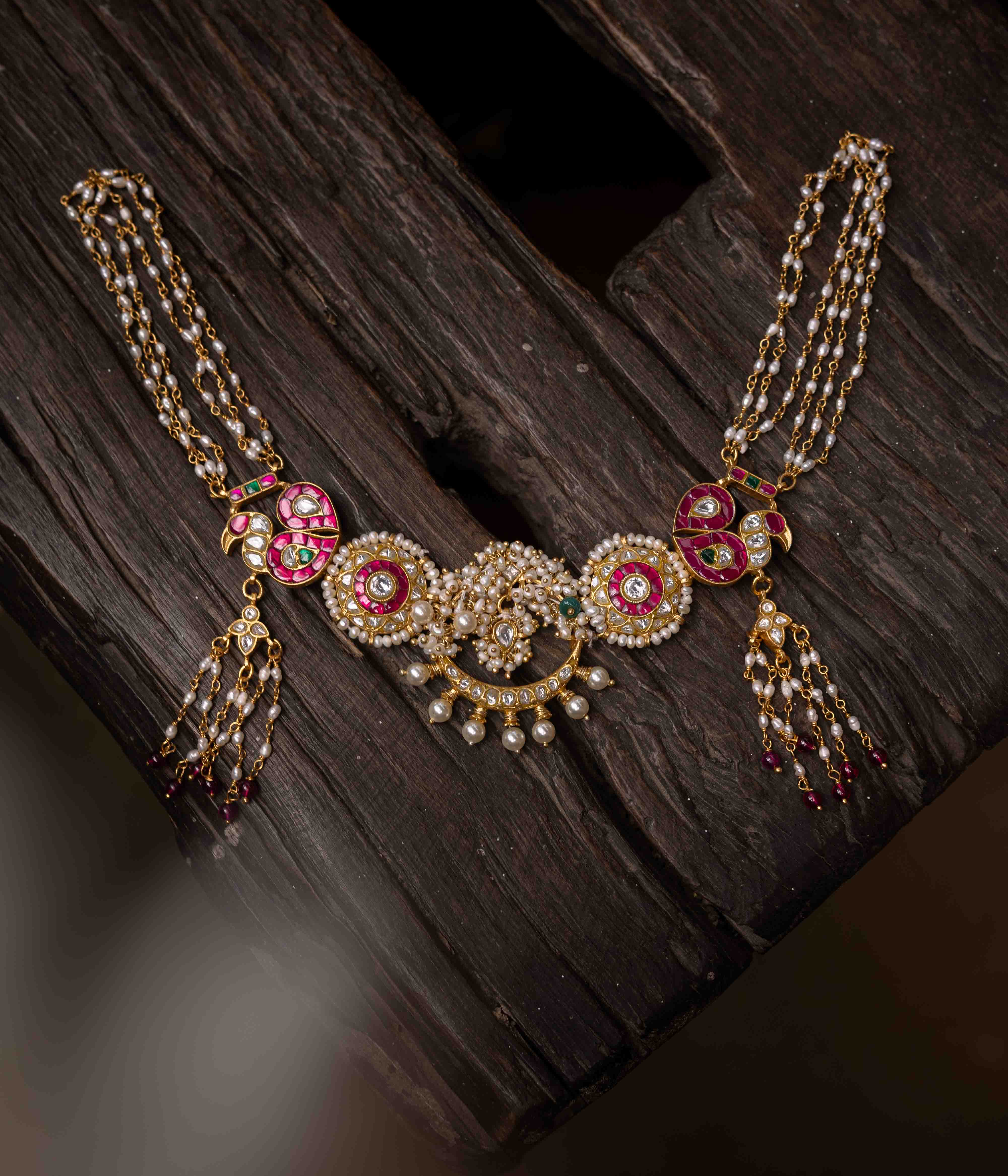 A multi-layered Kundan necklace with a central pendant and cascading strands of red beads and pearls.
