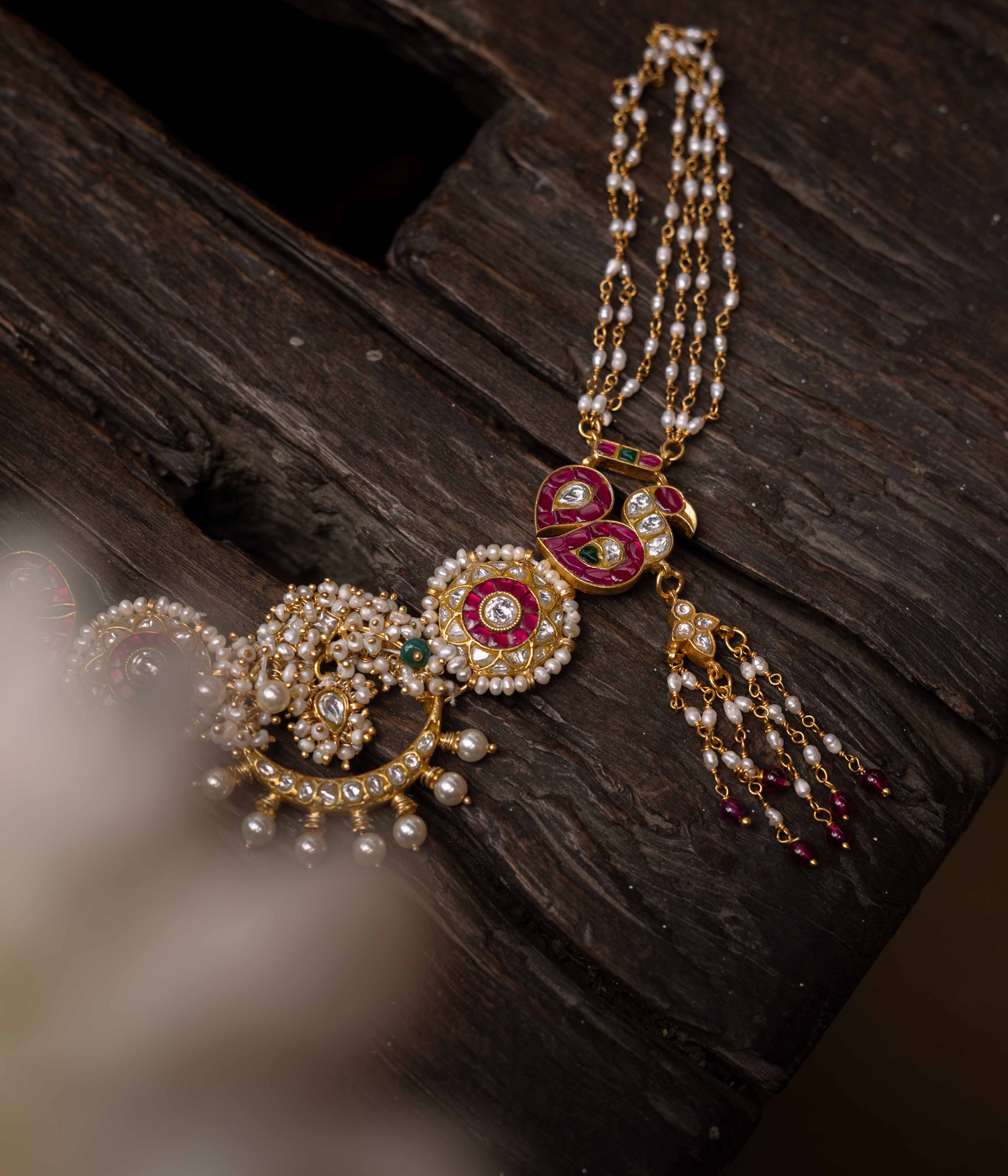 A multi-layered Kundan necklace with a central pendant and cascading strands of red beads and pearls.
