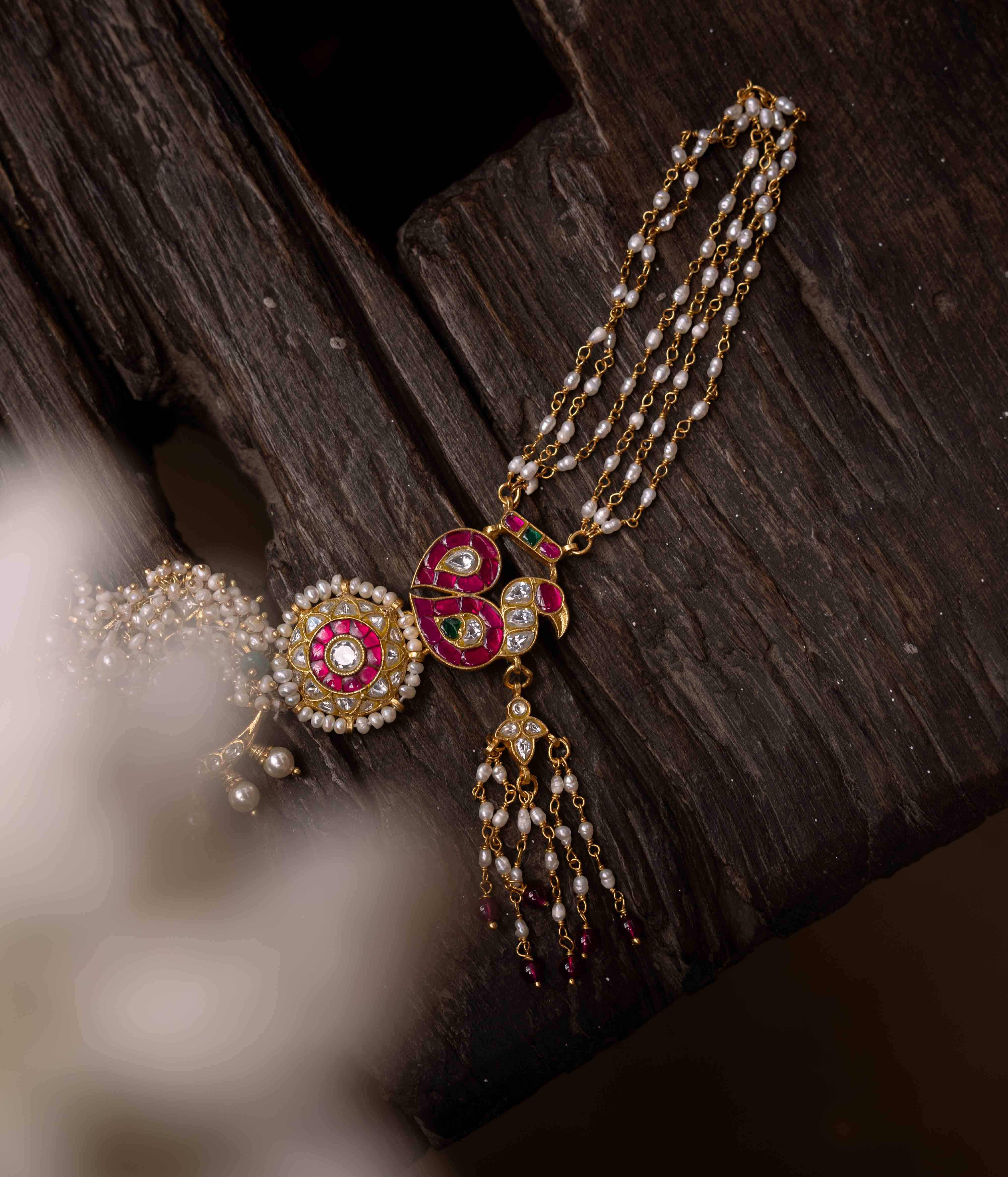 A multi-layered Kundan necklace with a central pendant and cascading strands of red beads and pearls.
