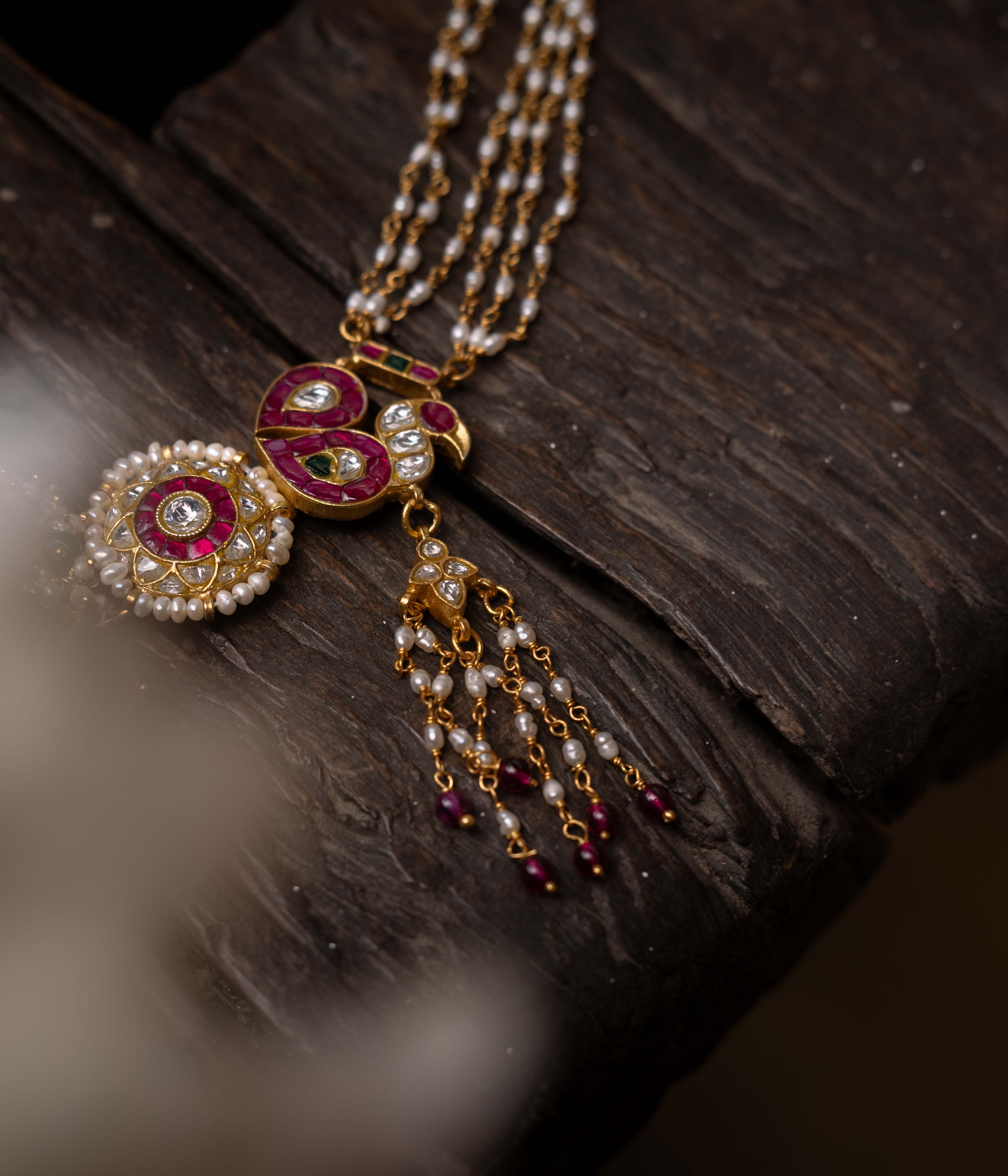 A multi-layered Kundan necklace with a central pendant and cascading strands of red beads and pearls.
