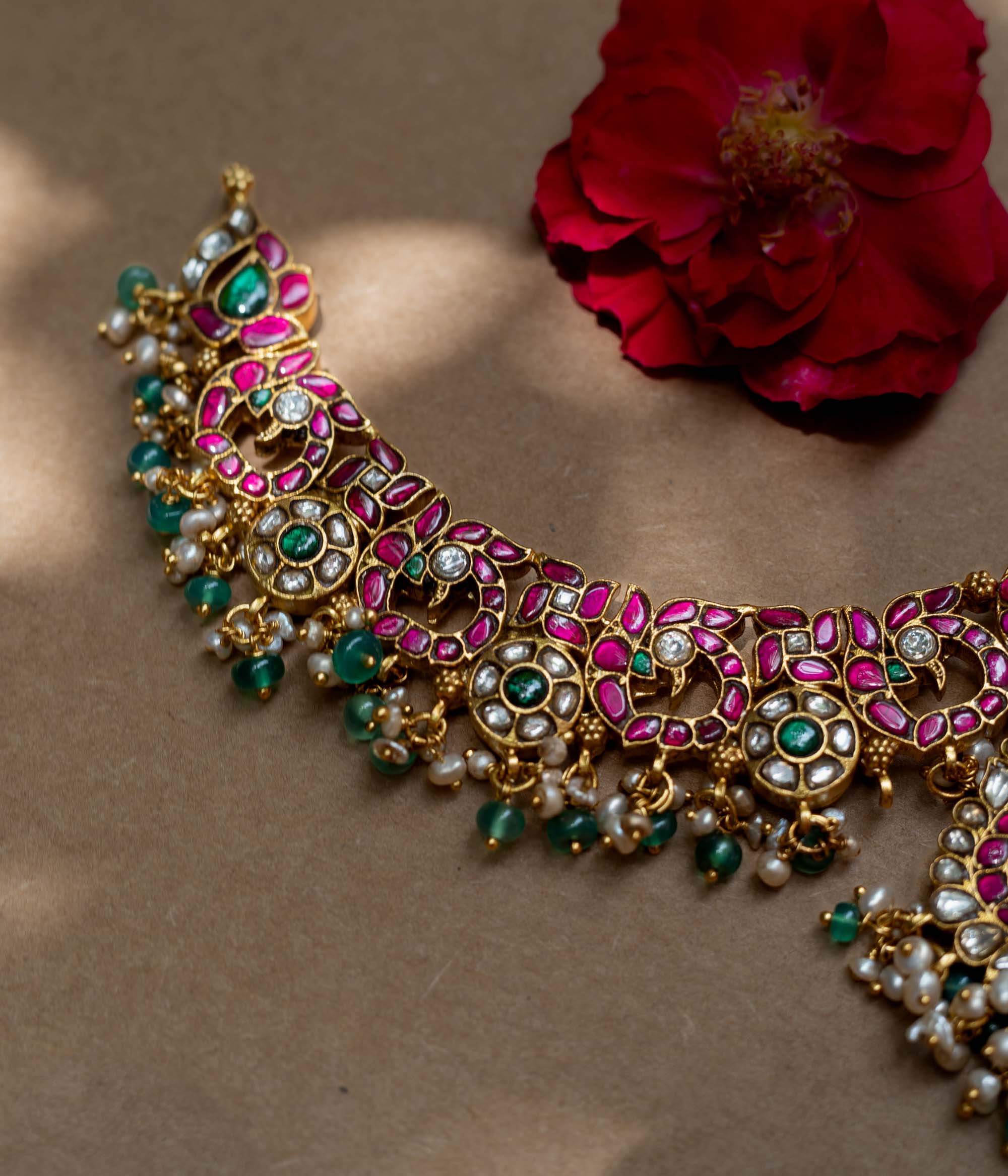 A handcrafted 22ct gold-plated 92.5 sterling silver Padmavati Kemp necklace, featuring red, green, and white Kundan stones, green beads, and pearls, with a broad, ornate design and a central pearl-clustered pendant, ideal for bridal wear and grand celebrations.