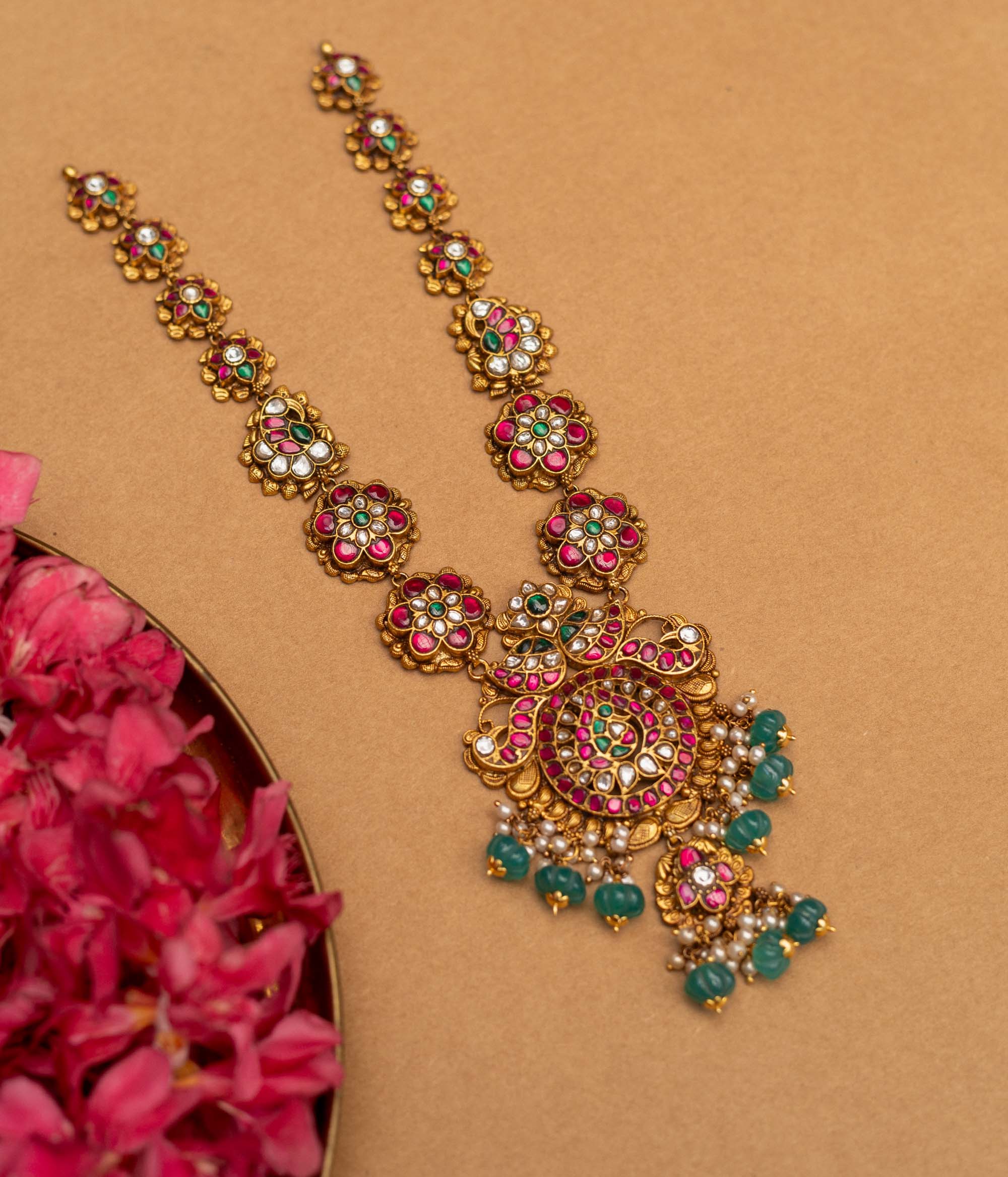 A 92.5 sterling silver Blossom Radiance Peacock Necklace with an antique finish, featuring a pendant adorned with twin peacocks, dazzling kundan stones, and vibrant pink and green accents, a floral-link chain, and dangling emerald-green beads and pearls, perfect for weddings, temple occasions, and cultural festivities.