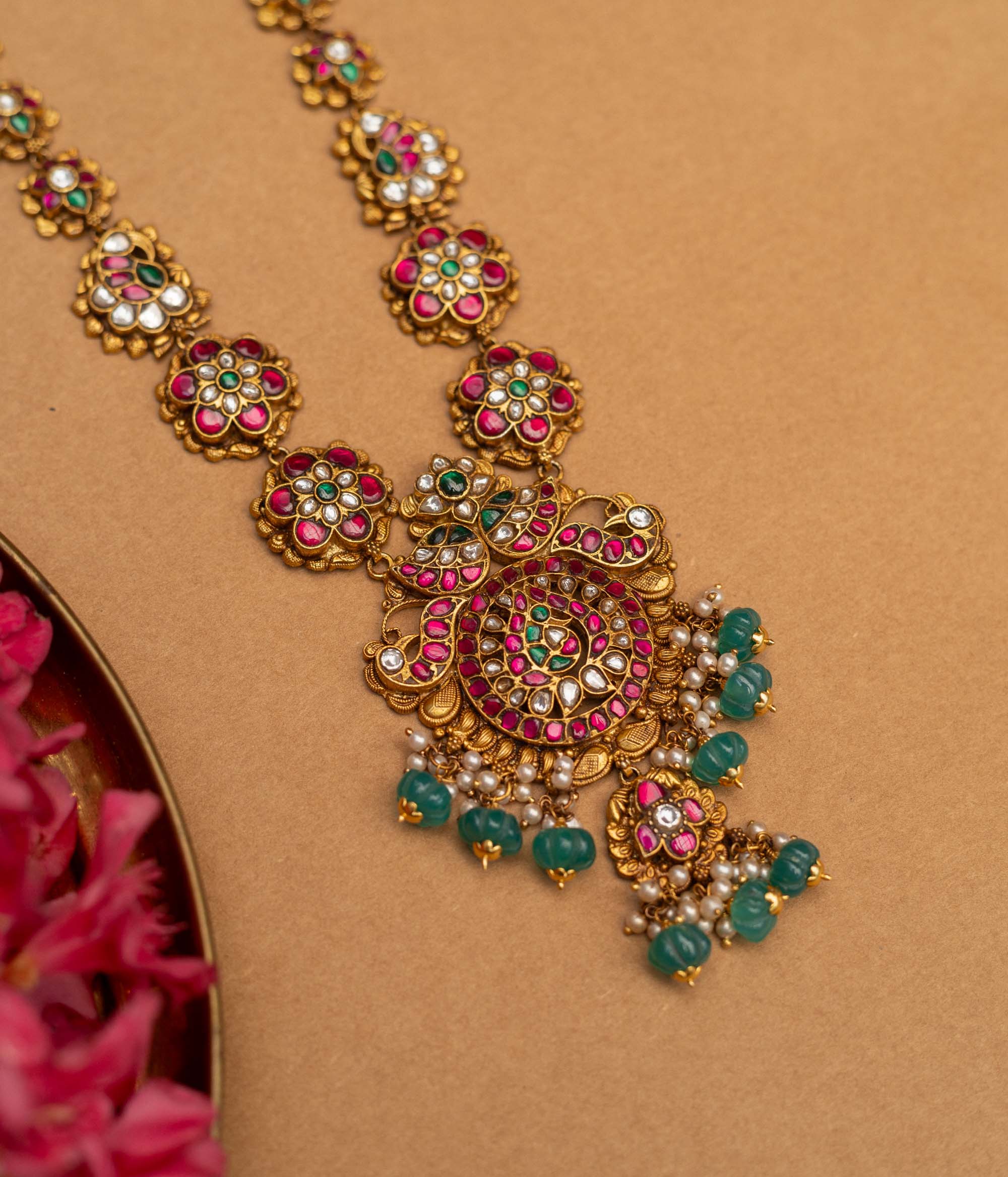 A 92.5 sterling silver Blossom Radiance Peacock Necklace with an antique finish, featuring a pendant adorned with twin peacocks, dazzling kundan stones, and vibrant pink and green accents, a floral-link chain, and dangling emerald-green beads and pearls, perfect for weddings, temple occasions, and cultural festivities.