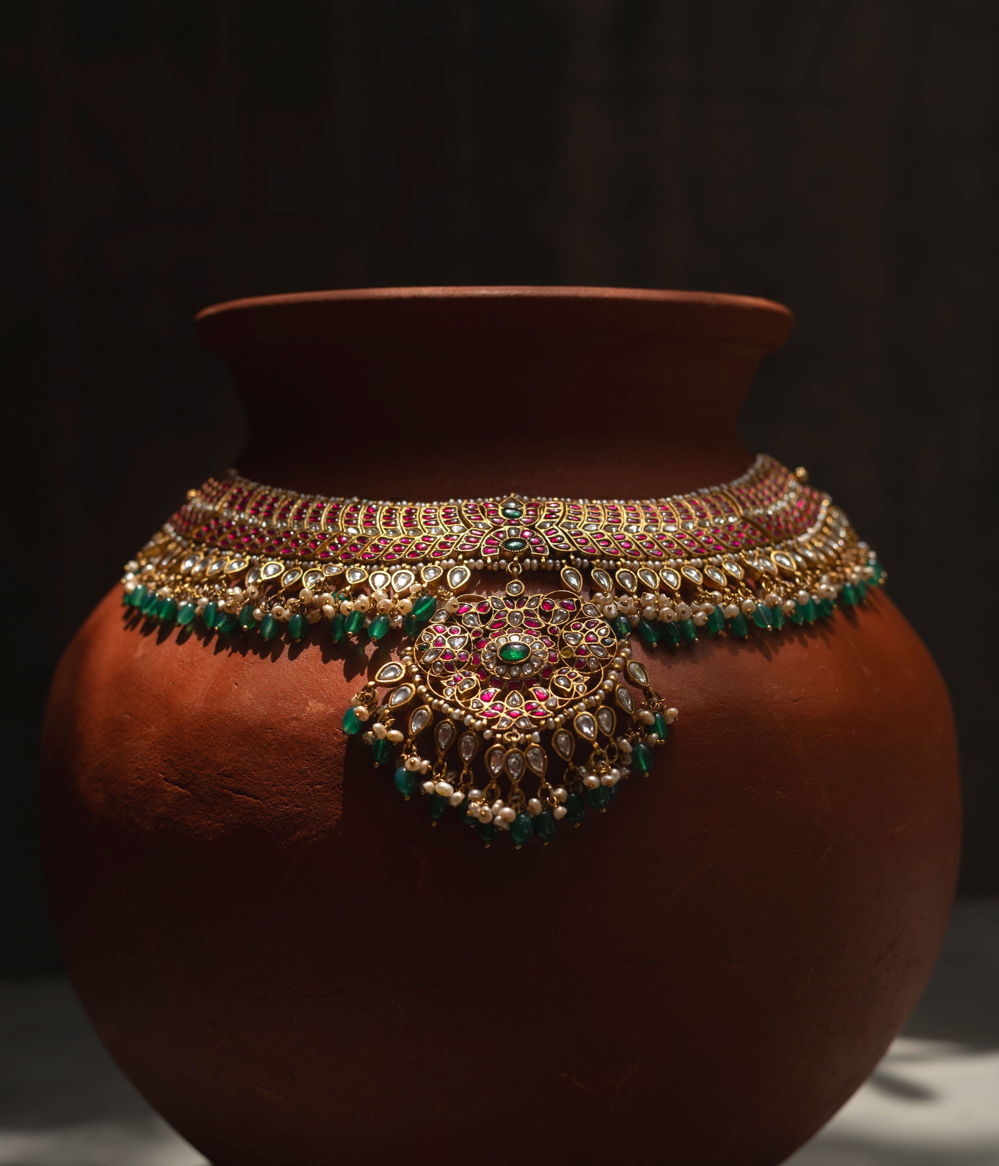A handcrafted 22ct gold-plated 92.5 sterling silver Rajsi Kemp Choker, featuring red, green, and white Kundan stones, red beads, and pearls, with a broad, ornate design and a central pearl-clustered pendant, ideal for bridal wear and grand celebrations.
