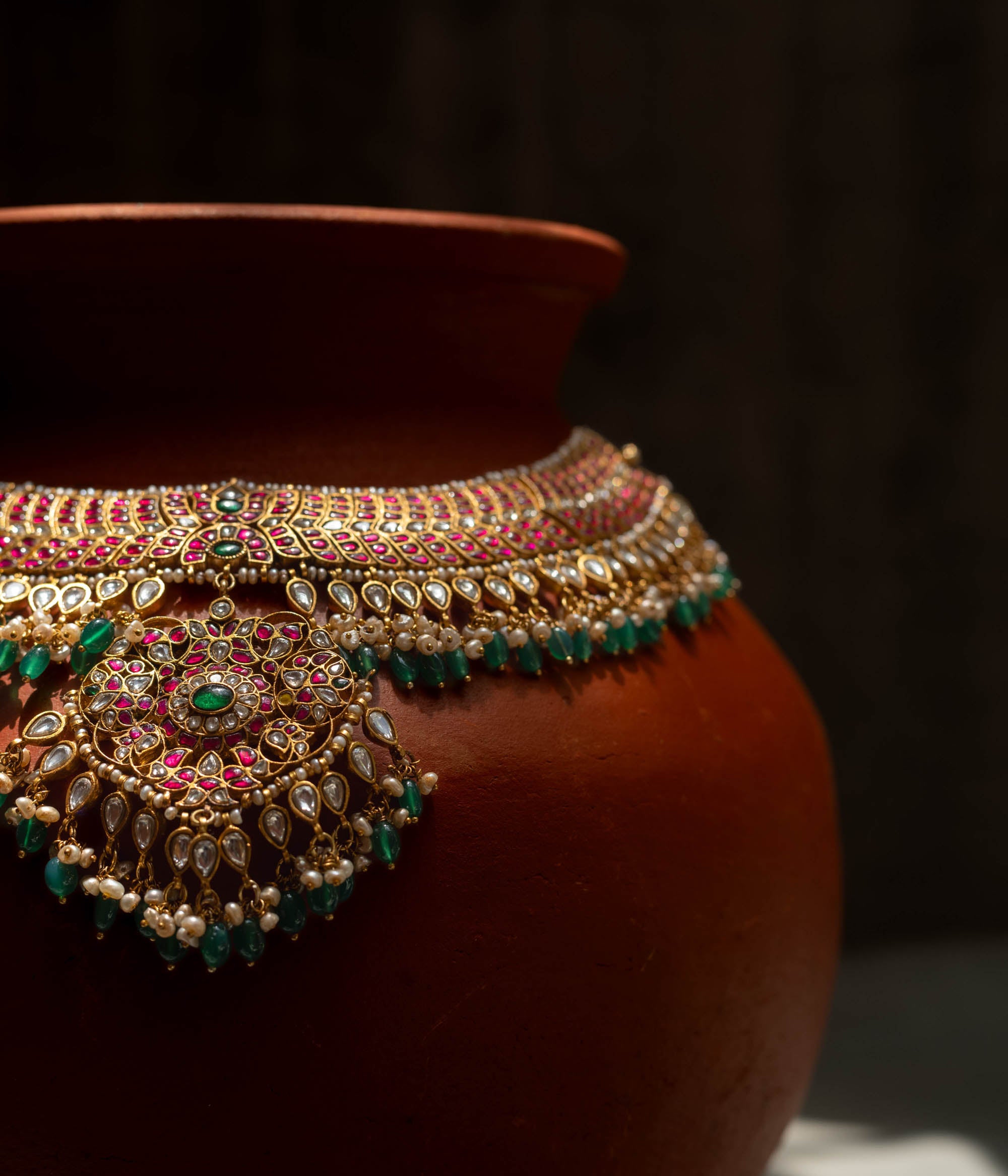 A handcrafted 22ct gold-plated 92.5 sterling silver Rajsi Kemp Choker, featuring red, green, and white Kundan stones, red beads, and pearls, with a broad, ornate design and a central pearl-clustered pendant, ideal for bridal wear and grand celebrations.