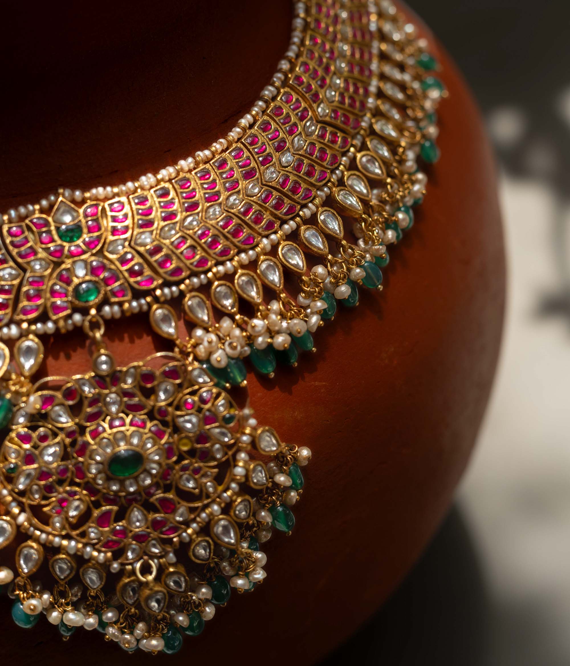 A handcrafted 22ct gold-plated 92.5 sterling silver Rajsi Kemp Choker, featuring red, green, and white Kundan stones, red beads, and pearls, with a broad, ornate design and a central pearl-clustered pendant, ideal for bridal wear and grand celebrations.
