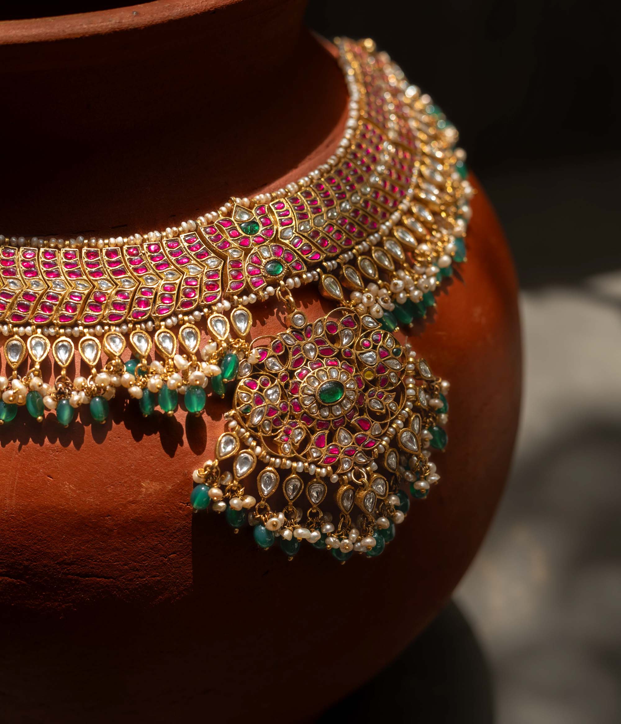 A handcrafted 22ct gold-plated 92.5 sterling silver Rajsi Kemp Choker, featuring red, green, and white Kundan stones, red beads, and pearls, with a broad, ornate design and a central pearl-clustered pendant, ideal for bridal wear and grand celebrations.