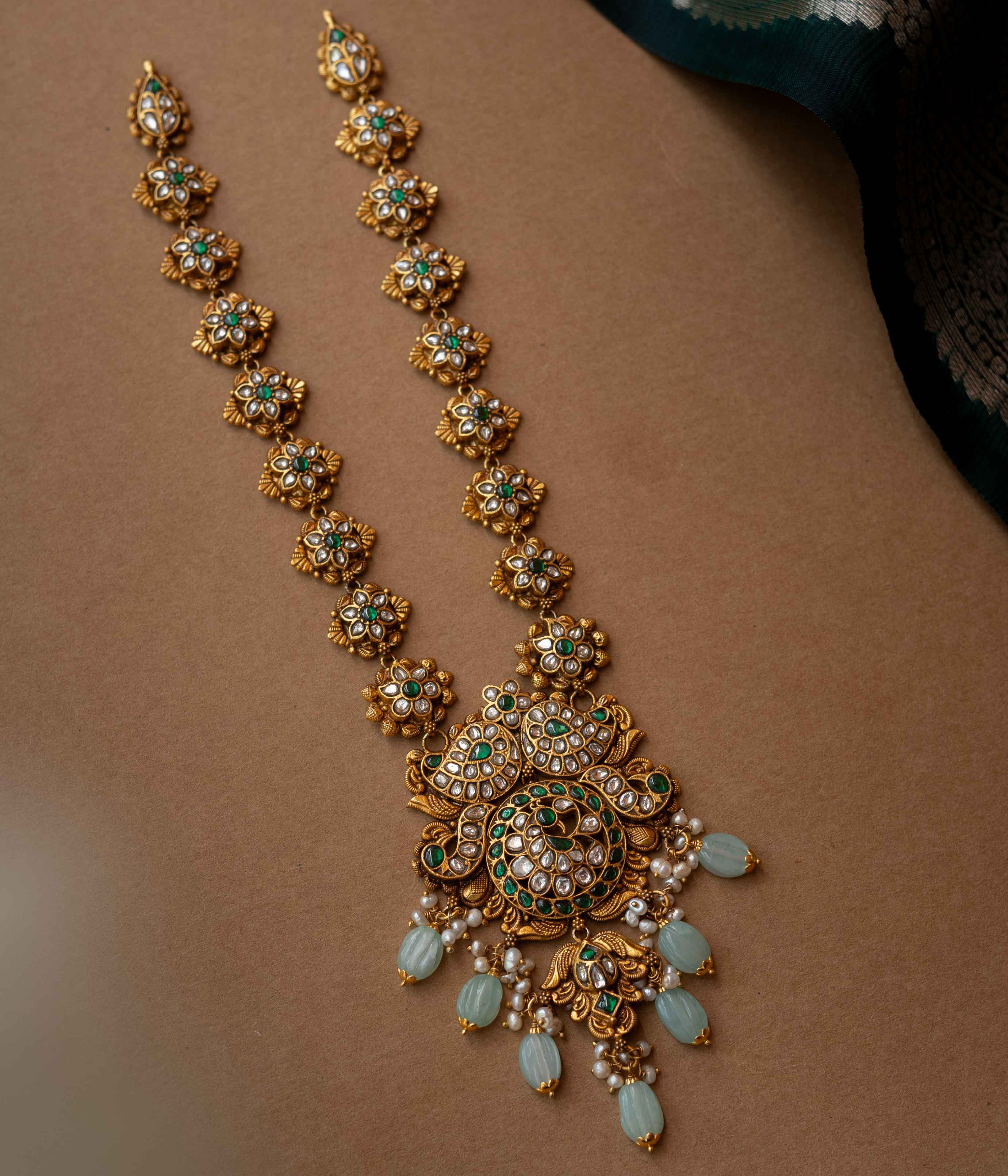 A multi-layered necklace with a central Kundan pendant and cascading strands of pearls and beads.
