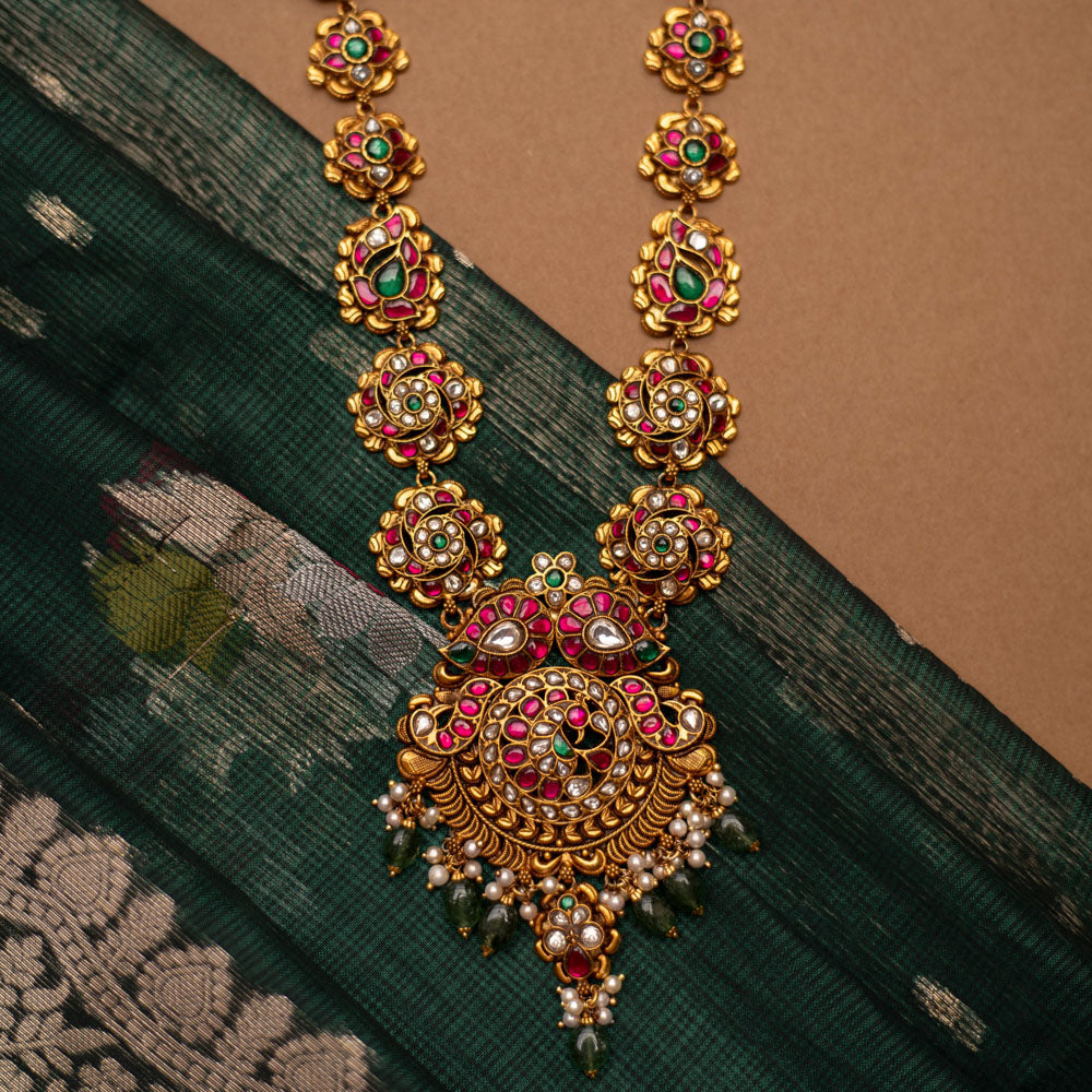 Close-up of a Kundan necklace with pearls and gems. The necklace is displayed on a brown bust against a blurred background.