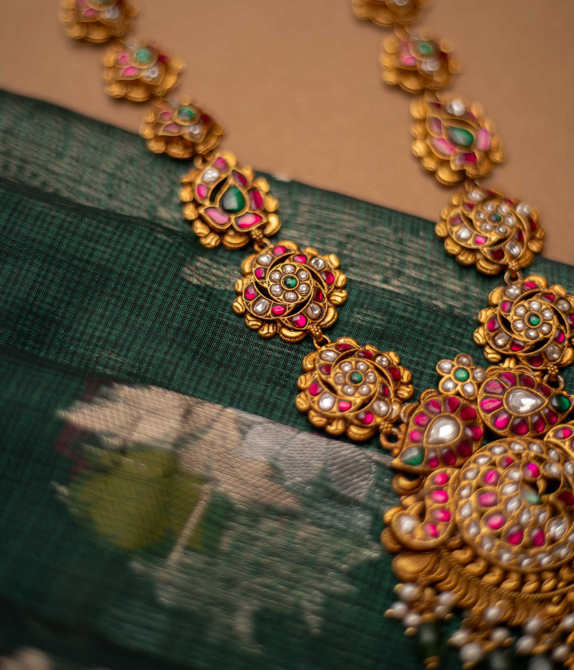 Close-up of a Kundan necklace with pearls and gems. The necklace is displayed on a brown bust against a blurred background.